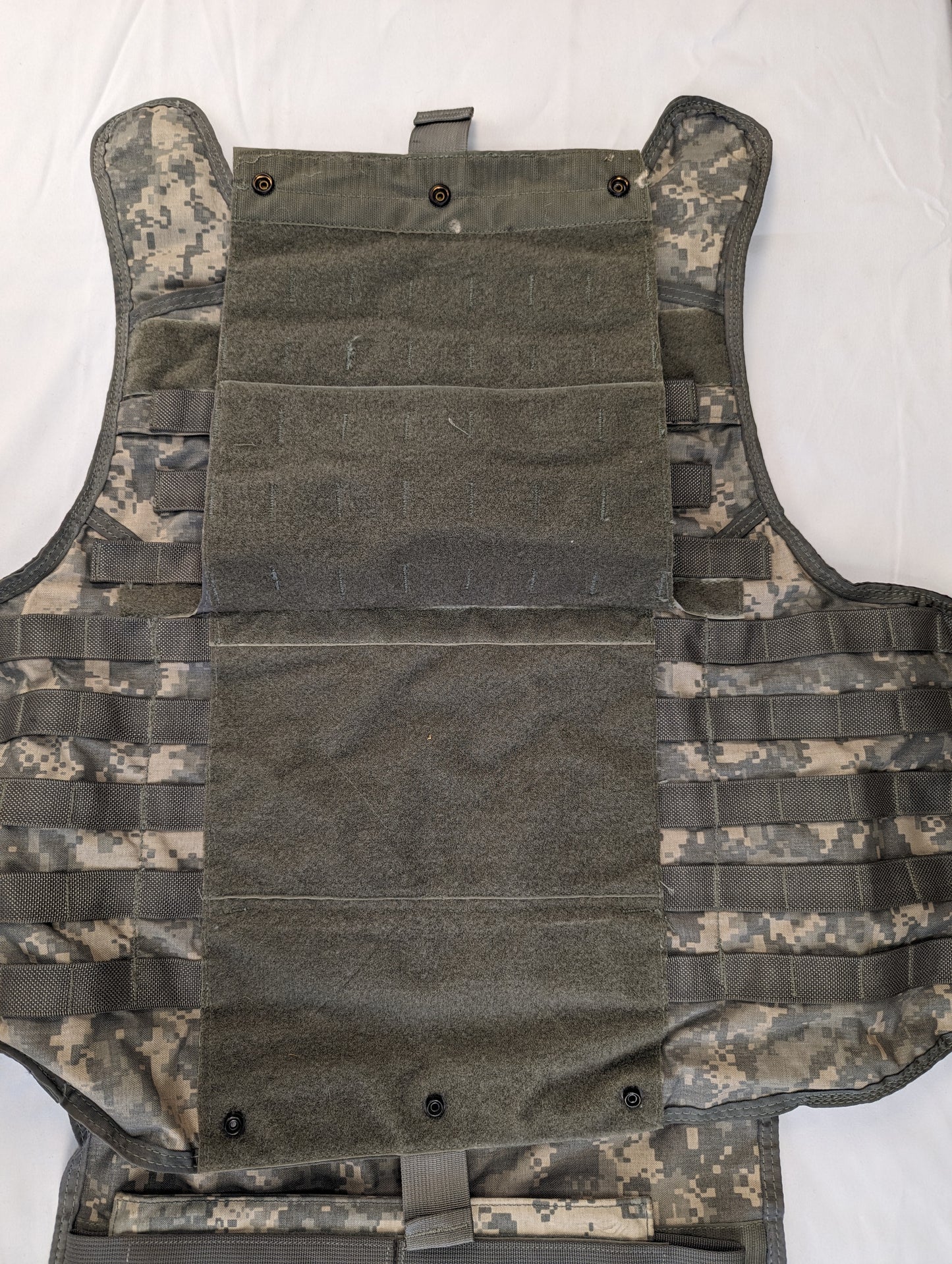 A close-up front view of the ACU camouflage IOTV, displaying the large central hook-and-loop field over the plate pocket, and the horizontal MOLLE webbing sewn onto it.