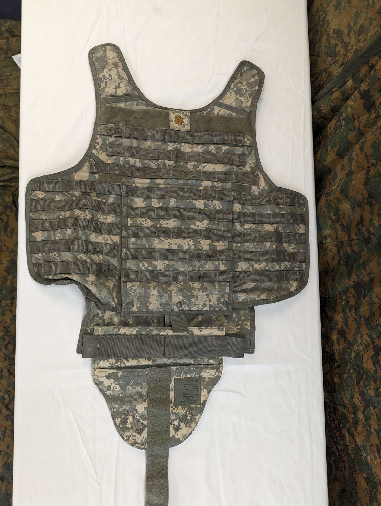 A large Improved Outer Tactical Vest (IOTV) in ACU digital camouflage, displayed flat on a white background, highlighting the MOLLE webbing, quick-release system, and lower torso protection flap.