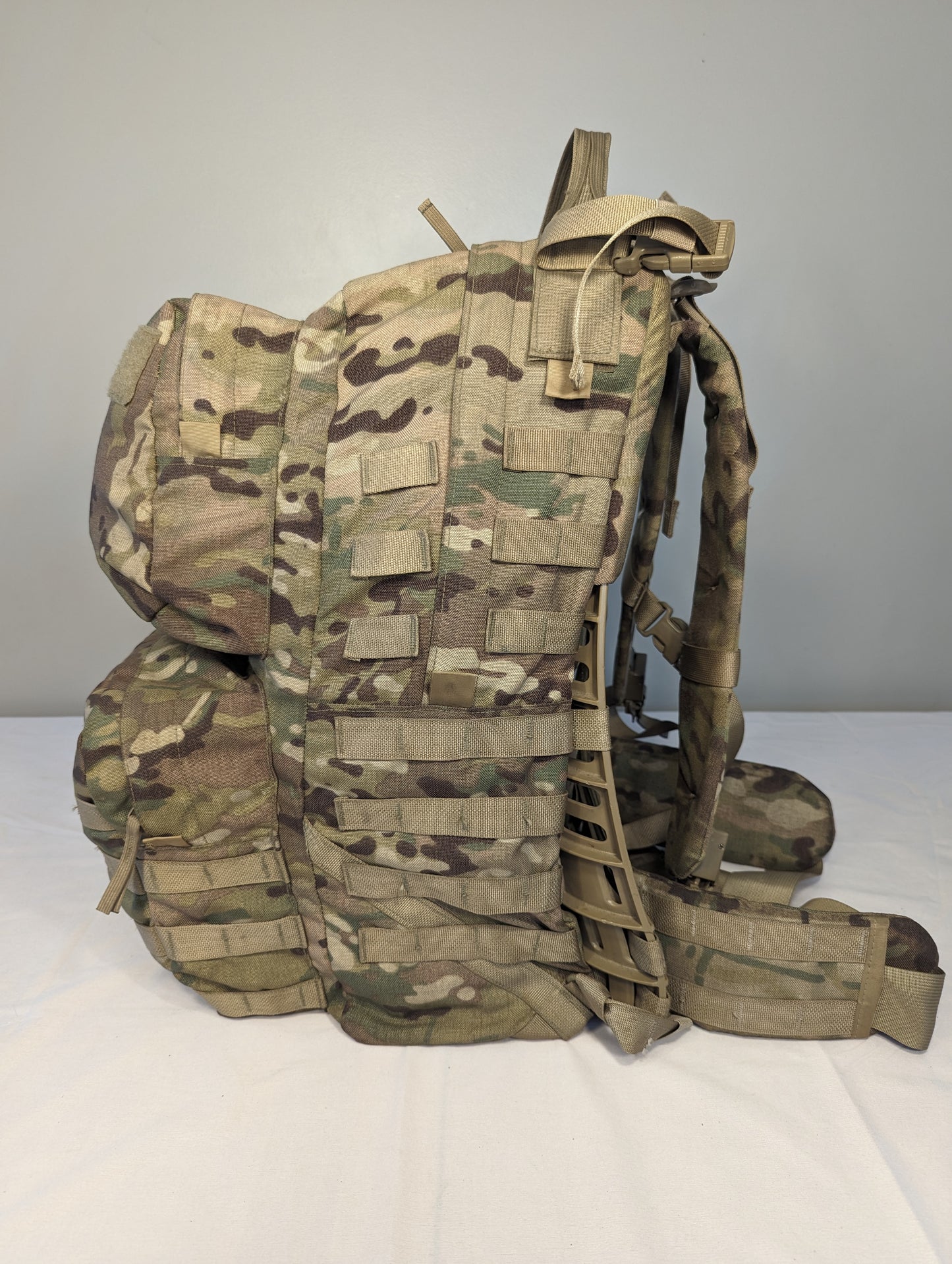 A heavily loaded U.S. Military Surplus Medium Field Pack Rucksack in OCP/Multicam camouflage, viewed from the side, showcasing its wide profile, attached pouches, and complete MOLLE suspension system.