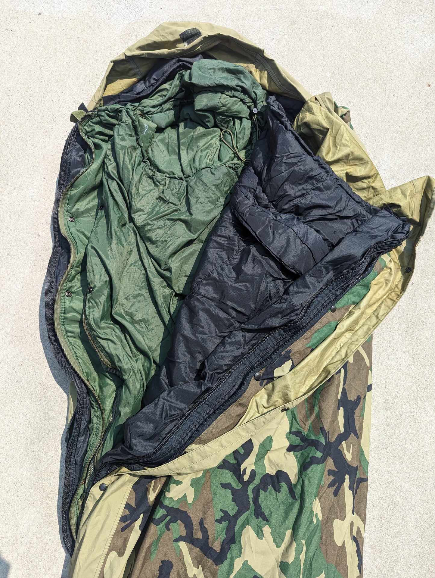 A full view of the U.S. Military Modular Sleep System (MSS) laid open, demonstrating the three-layer system with the black, olive green, and Woodland camouflage bags nested together.