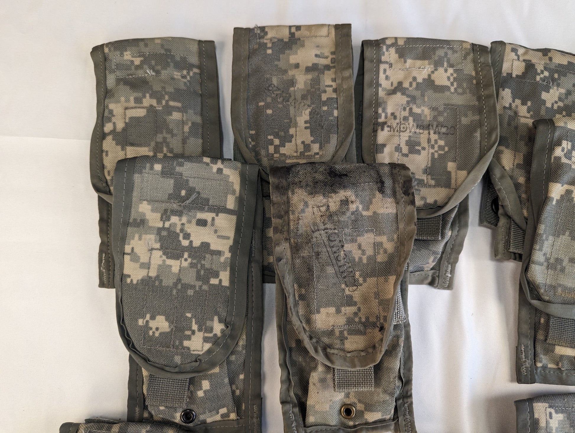 A close-up studio shot of a cluster of overlapping U.S. Military Surplus 2-Mag Pouches in ACU digital camouflage, highlighting the flaps, snap closures, and worn fabric texture.