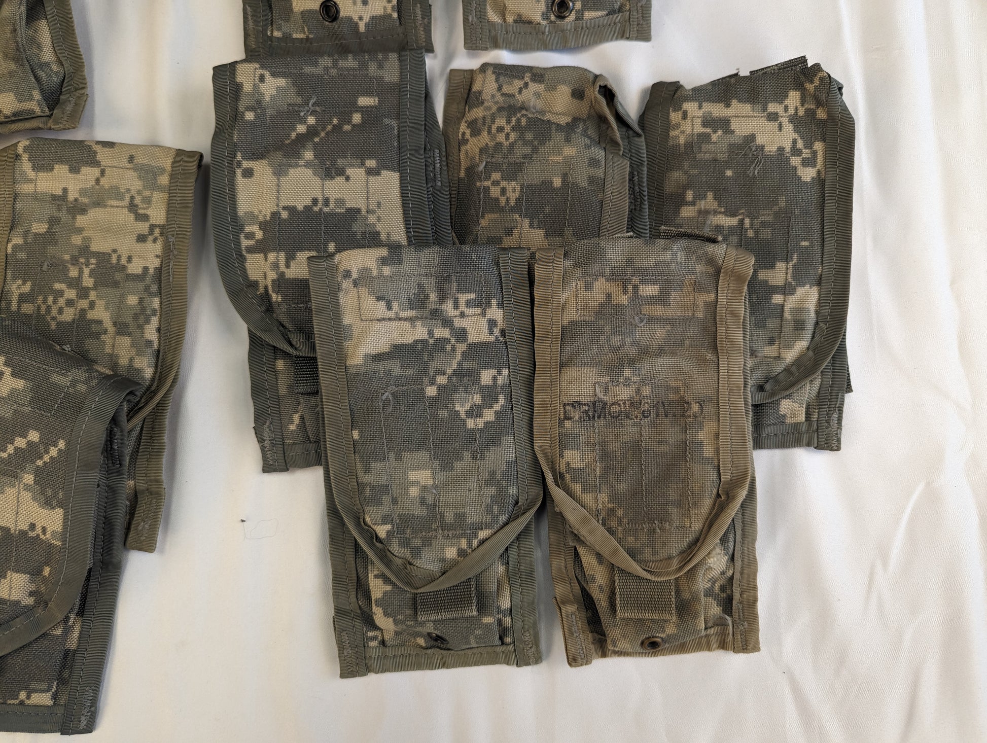 A close-up studio shot of a cluster of overlapping U.S. Military Surplus 2-Mag Pouches in ACU digital camouflage, highlighting the worn flaps, snap closures, and used fabric texture.