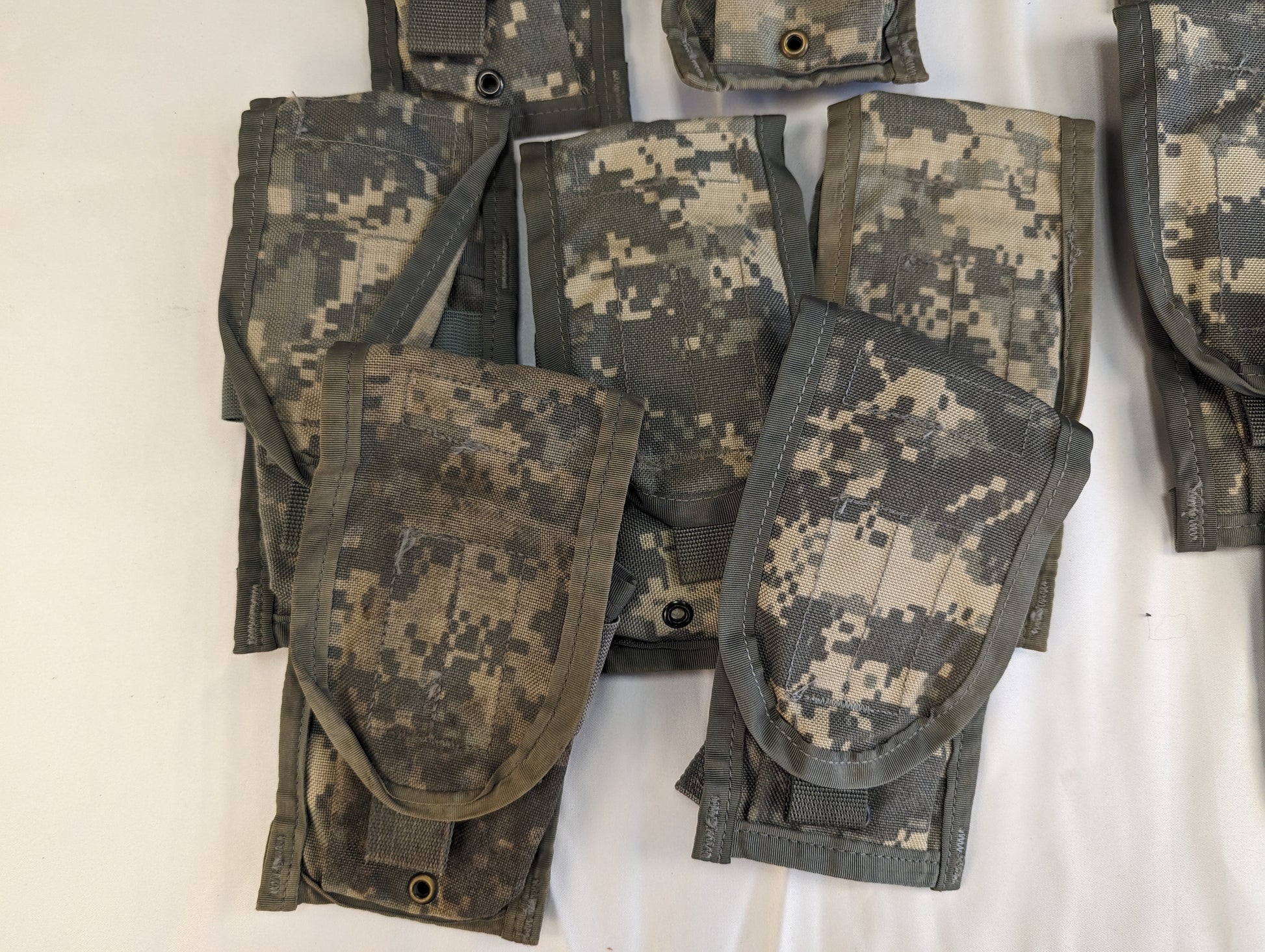 A close-up studio shot of a cluster of overlapping U.S. Military Surplus 2-Mag Pouches in ACU digital camouflage, highlighting the flaps, snap closures, and worn fabric texture.