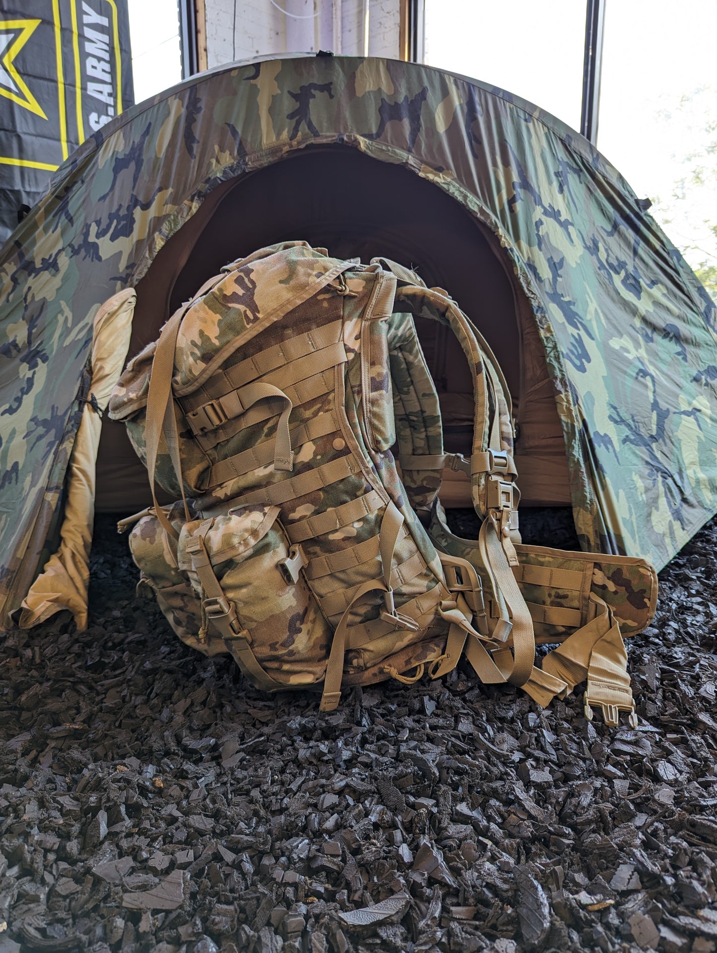 A dirty, field-used U.S. Military Surplus MOLLE 4000 Rucksack in OCP/Multicam camouflage lying on its side next to a partially set up U.S. Army camouflage tent.