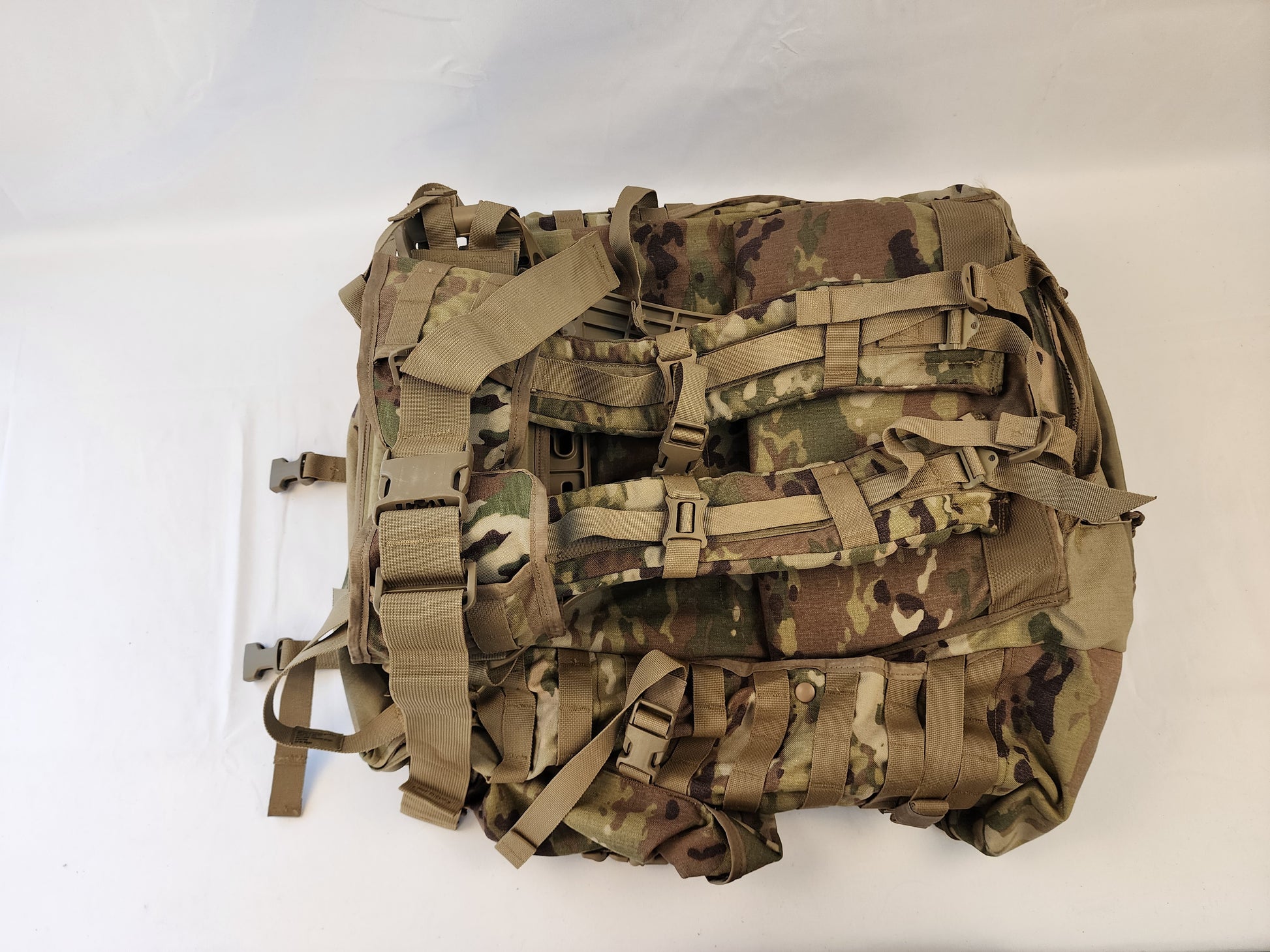 A large U.S. Military Surplus MOLLE 4000 Rucksack in OCP/Multicam camouflage, shown lying on its back, emphasizing the numerous horizontal MOLLE webbing loops and compression straps on the front panel.