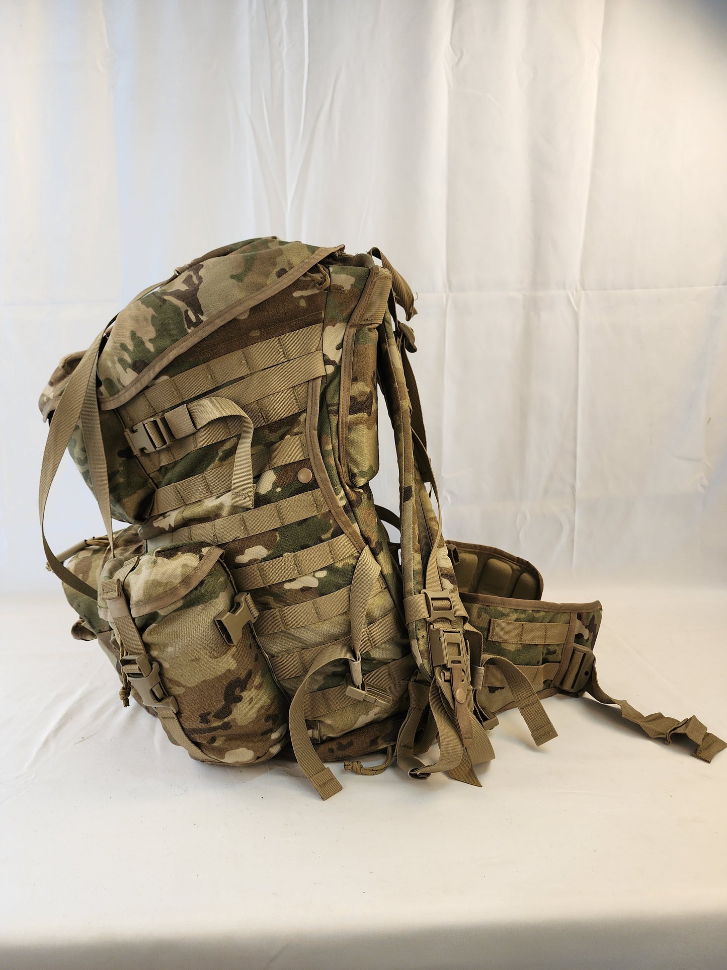 A large U.S. Military Surplus MOLLE 4000 Rucksack in OCP/Multicam camouflage, shown from a low side angle, highlighting the depth of the pack, the side webbing, and the fully padded hip belt.