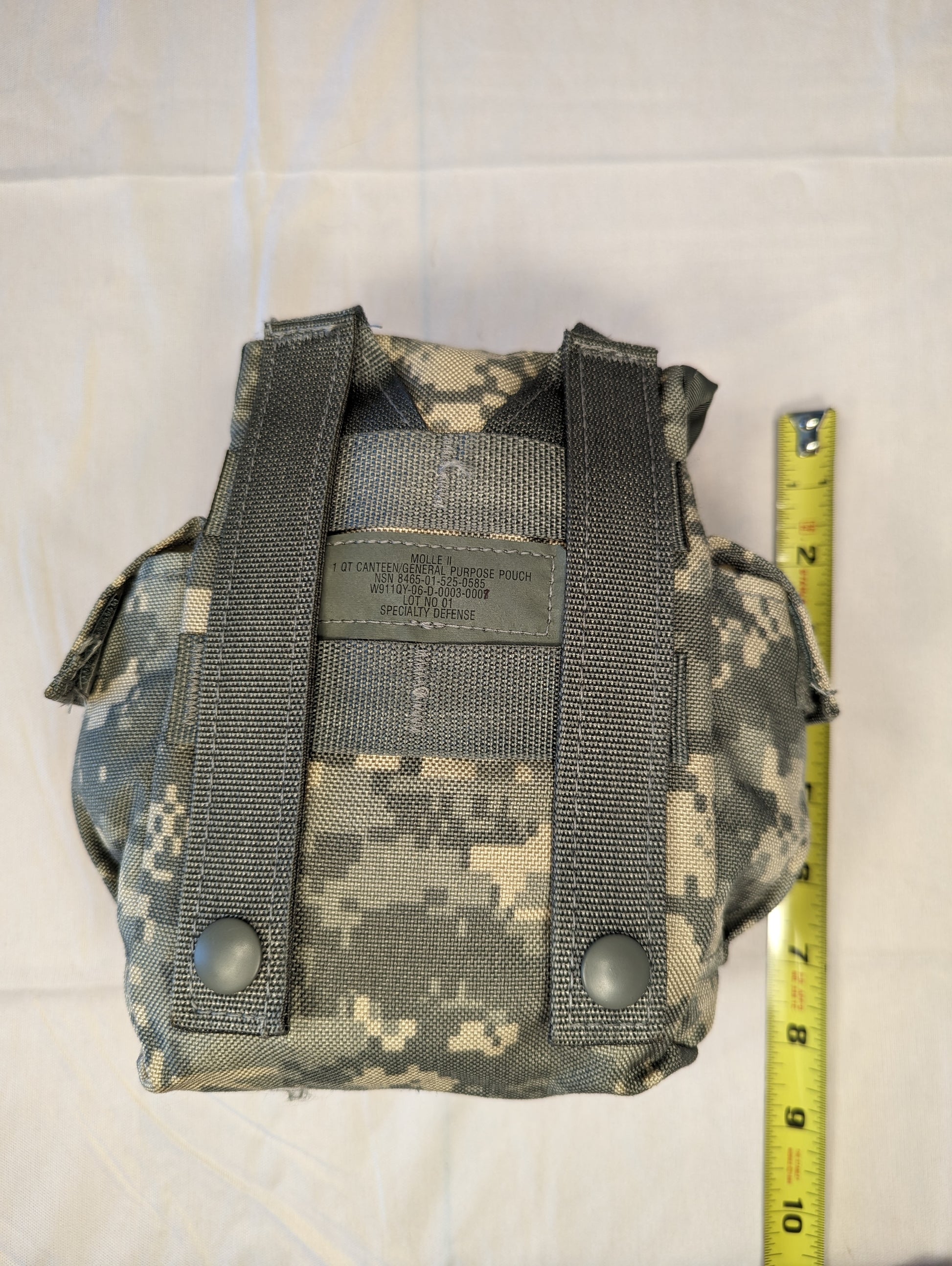 A back view of a U.S. Military Surplus MOLLE II 1-Quart Canteen/General Purpose Pouch in ACU digital camouflage, displaying the vertical MOLLE attachment straps and a yellow tape measure indicating the height.