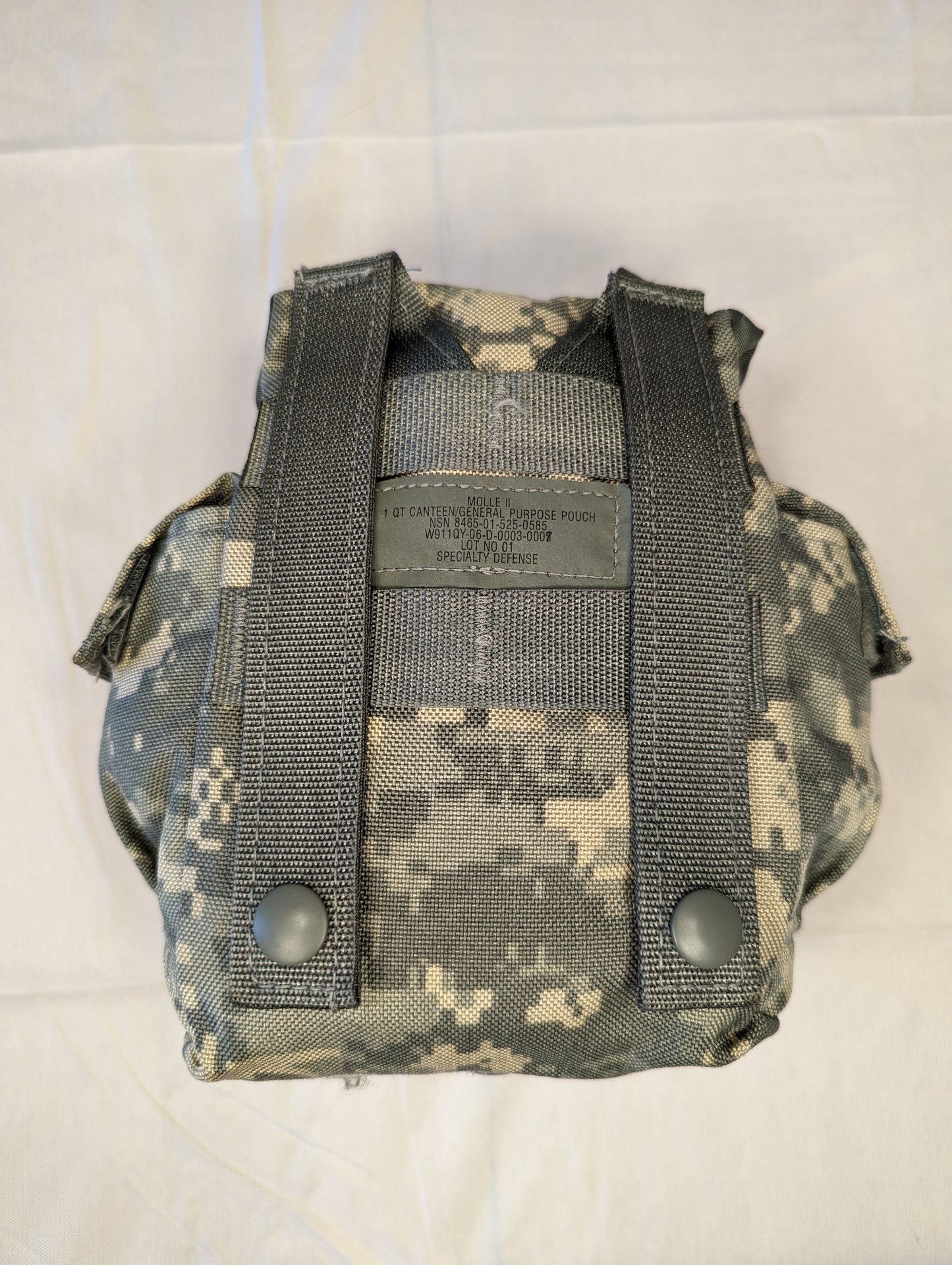 A back view of a U.S. Military Surplus MOLLE II 1-Quart Canteen/General Purpose Pouch in ACU digital camouflage, clearly displaying the two vertical MOLLE attachment straps, metal snap buttons, and the printed issue markings with NSN information.
