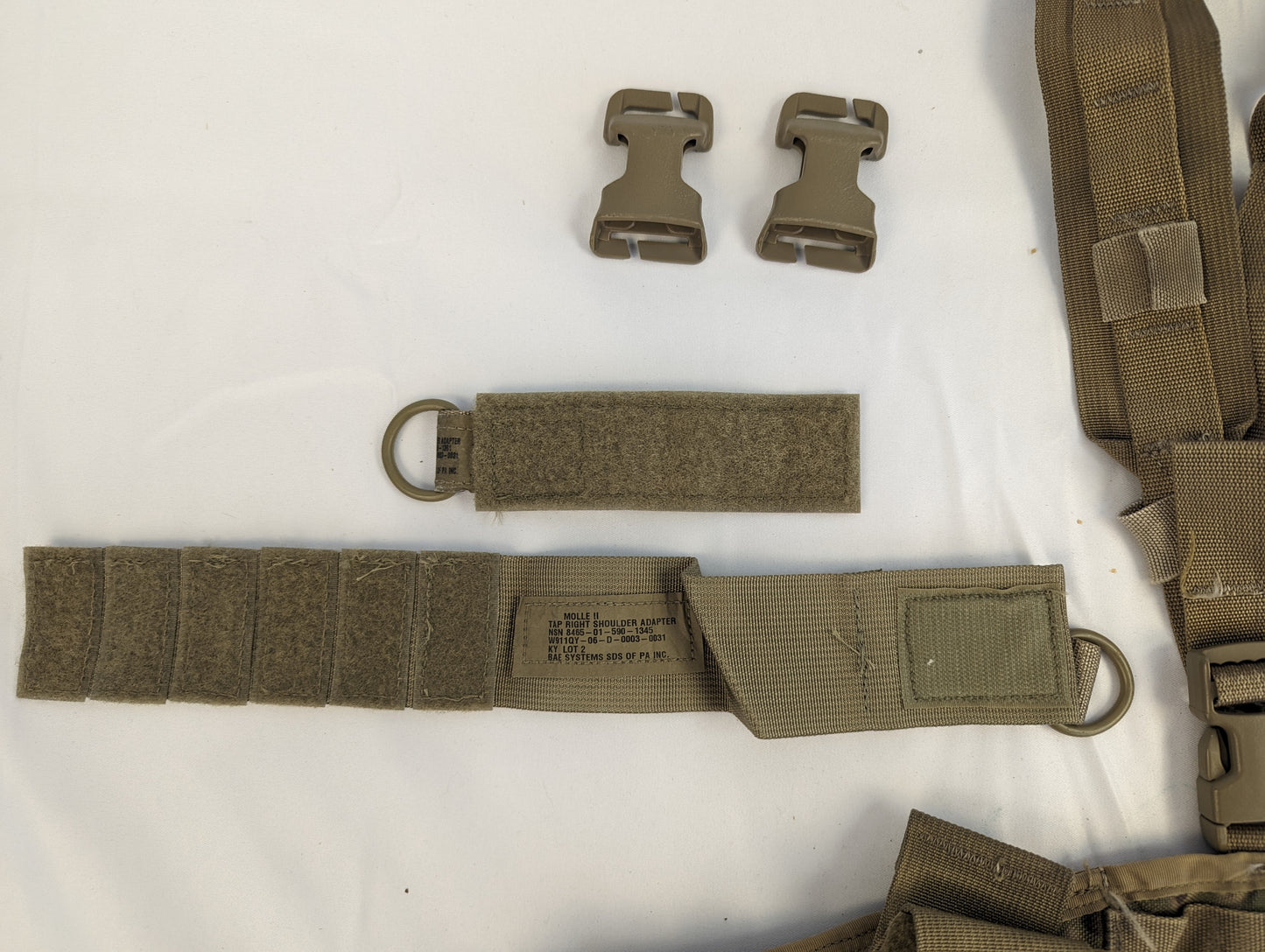 A close-up of tactical webbing components for a U.S. Military MOLLE system, featuring two quick-release plastic buckles and a coyote brown cummerbund strap assembly with hook-and-loop closure and a D-ring.