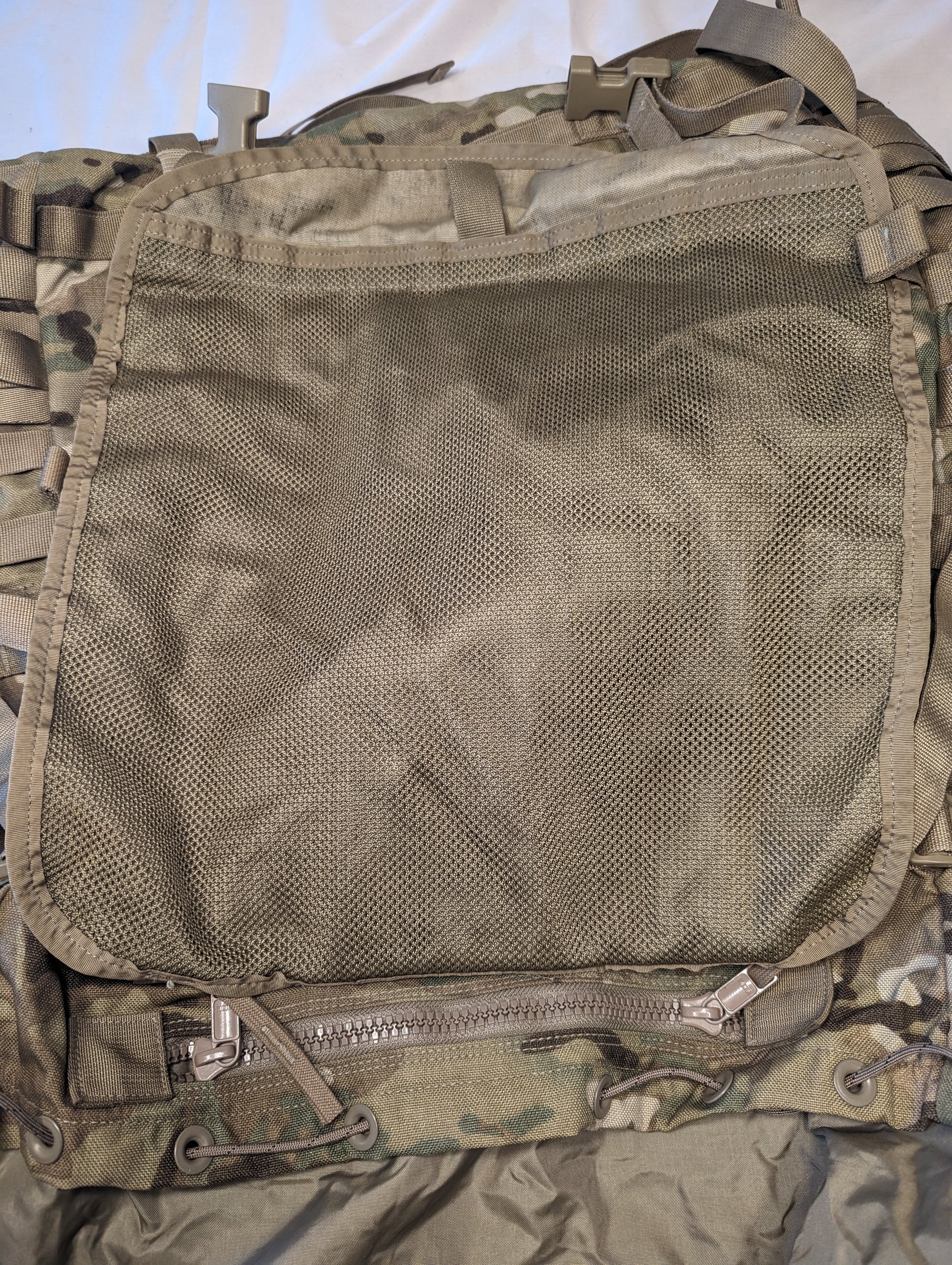 A close-up view of the interior organization panel of a U.S. Military MOLLE II Large Rucksack, showing a large, empty, zippered mesh pocket set against OCP/Multicam camouflage fabric.