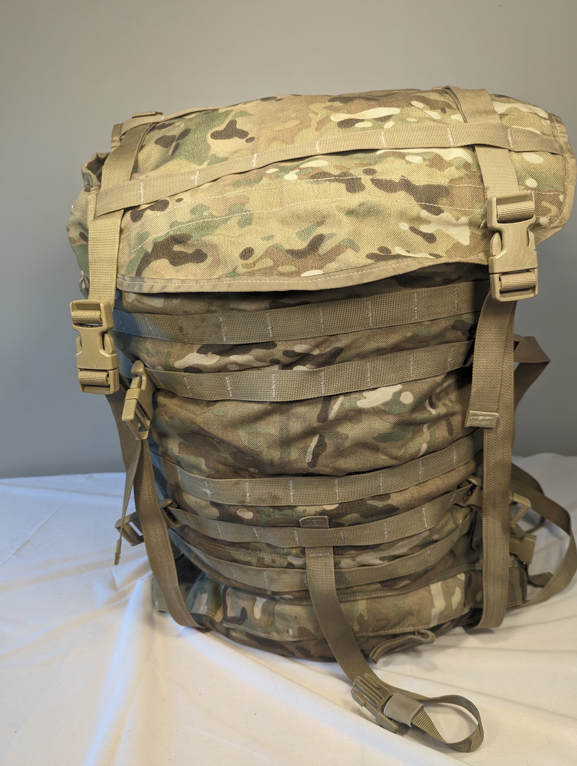 A U.S. Military Surplus MOLLE II Large Rucksack in OCP/Multicam camouflage, standing upright on a white surface, featuring extensive horizontal webbing, vertical compression straps, and a large top flap.