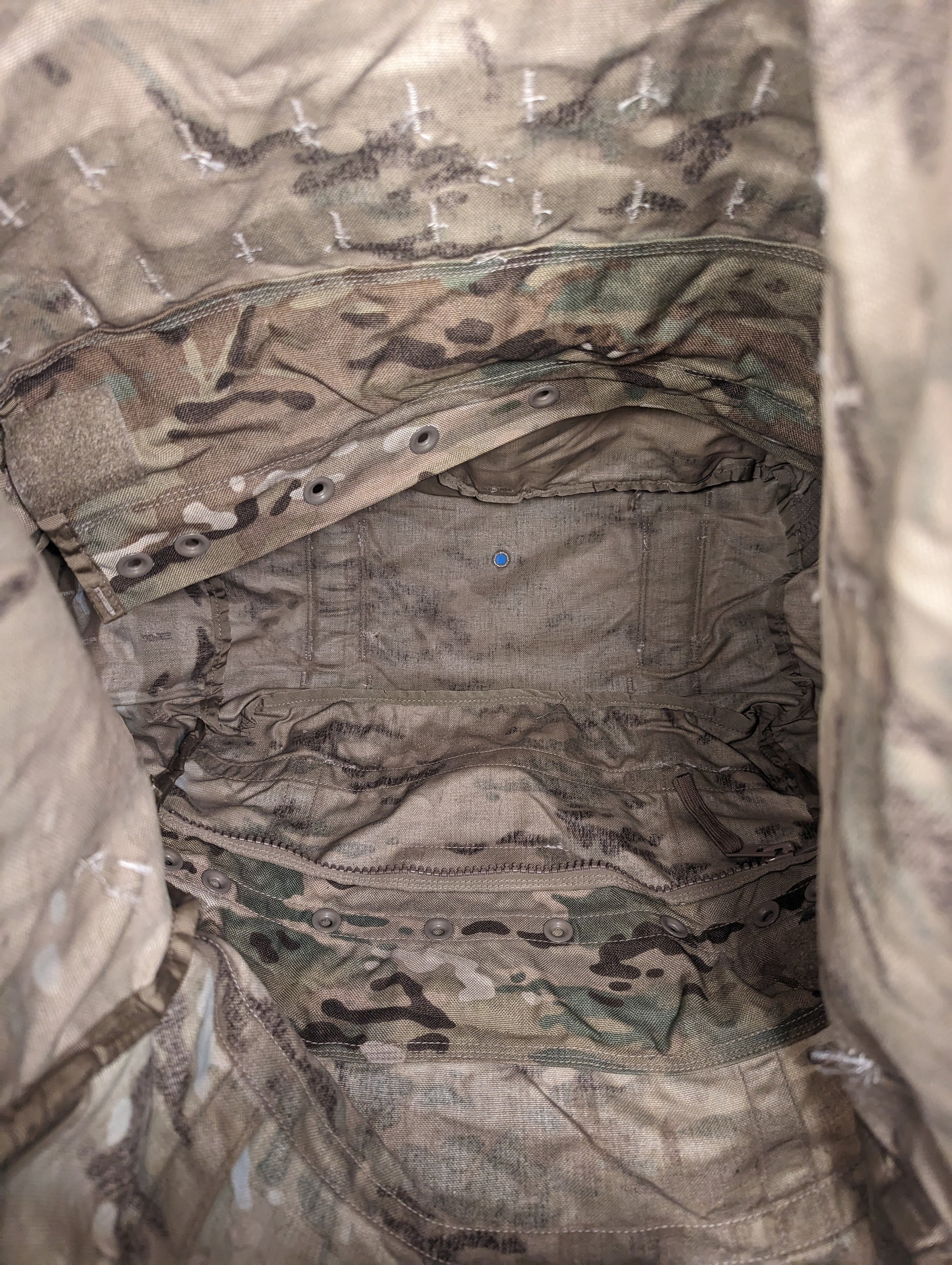 A close-up, top-down view into the open main compartment of a U.S. Military Surplus MOLLE II Large Rucksack in OCP/Multicam camouflage, revealing the internal radio pocket and drawstring storm collar.