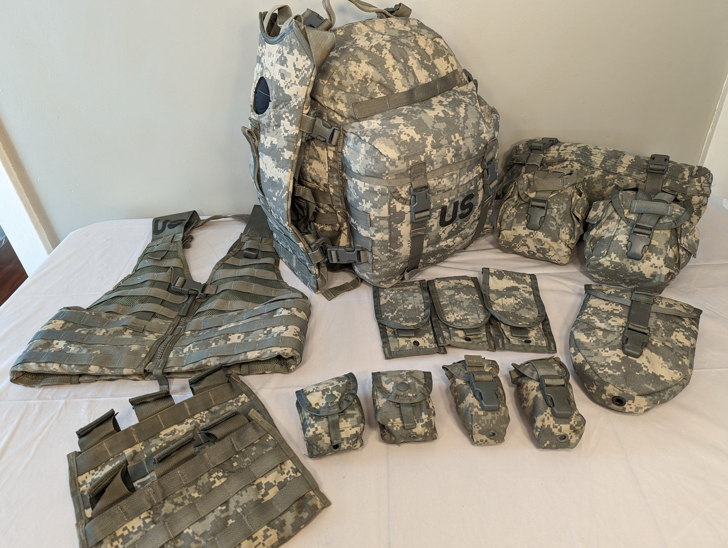 An overhead flat lay photograph of a complete U.S. Military MOLLE II Rifleman Set in ACU digital camouflage. The set includes a vest, a large rucksack with a 'US' stencil, and numerous detached magazine and utility pouches.