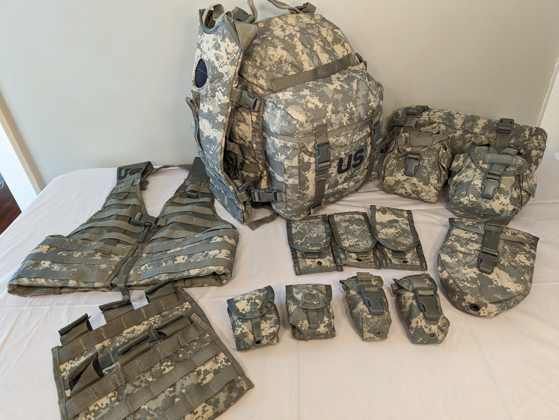 An overhead flat lay photograph of a complete U.S. Military MOLLE II Rifleman Set in ACU digital camouflage. The set includes a vest, a large rucksack with a 'US' stencil, and numerous detached magazine and utility pouches.