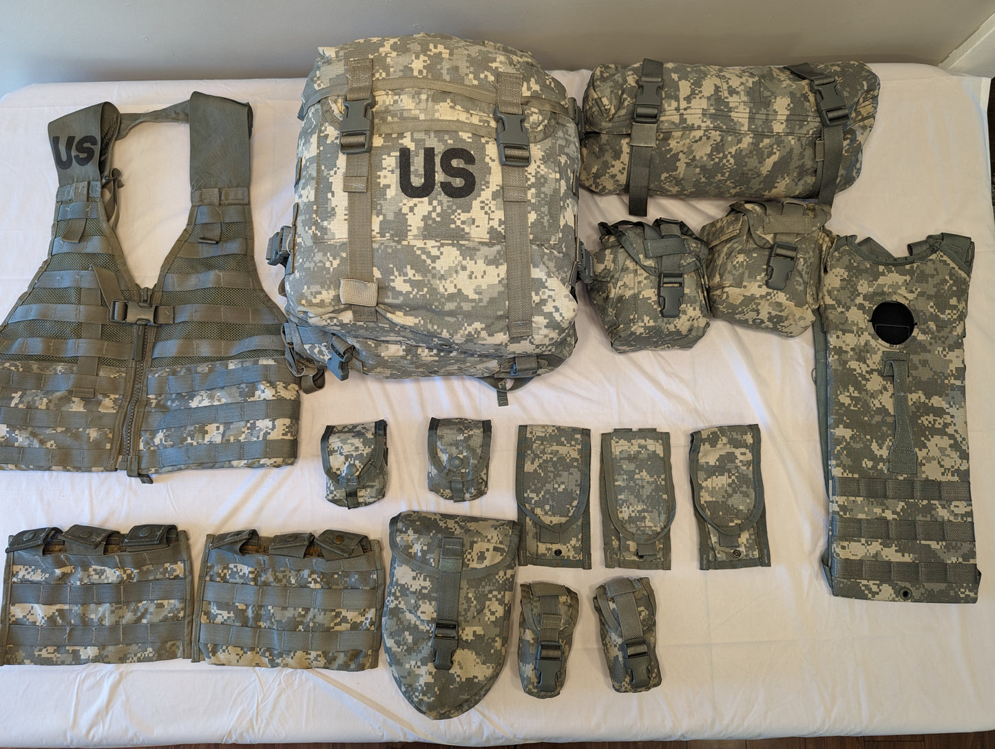 An overhead flat lay photograph of a complete U.S. Military MOLLE II Rifleman Set in ACU digital camouflage. The set includes a vest, a large rucksack with a 'US' stencil, and numerous attached and detached accessory pouches.