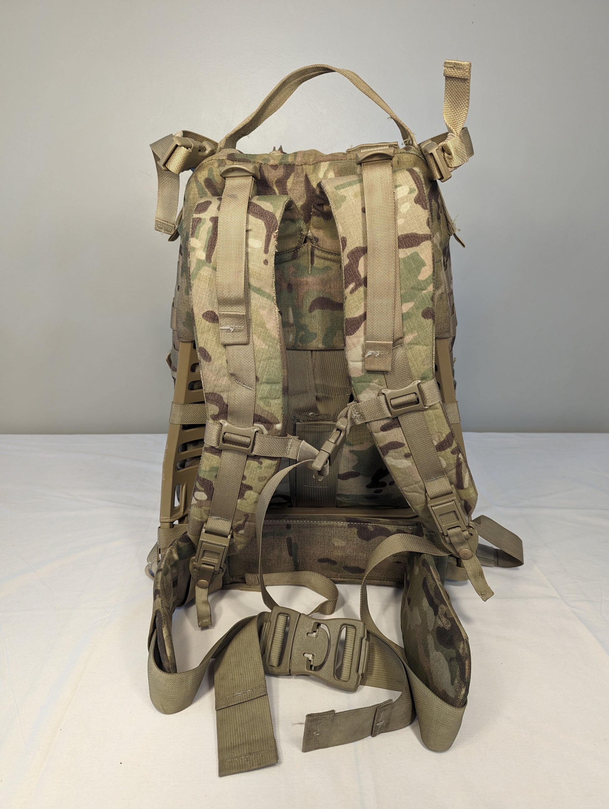 A close-up back view of a U.S. Military Surplus MOLLE II Rucksack suspension system in OCP/Multicam camouflage, highlighting the padded shoulder straps, hip belt, and webbing attachment points.