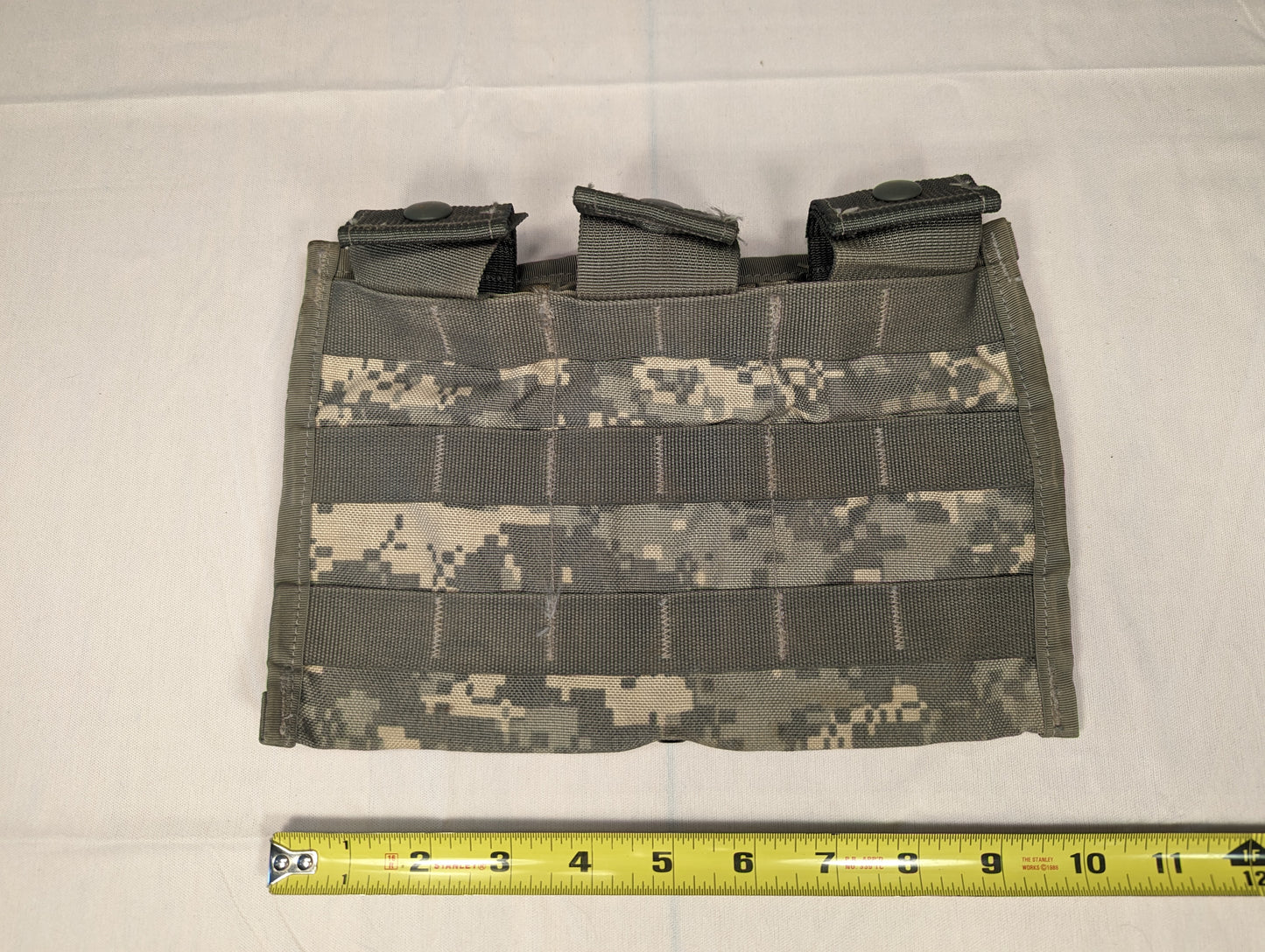 A single U.S. Military Surplus Triple Magazine Pouch in ACU digital camouflage, laid flat, featuring three side-by-side cells with snap-button flaps, dense horizontal MOLLE webbing, and a tape measure at the base demonstrating its width.