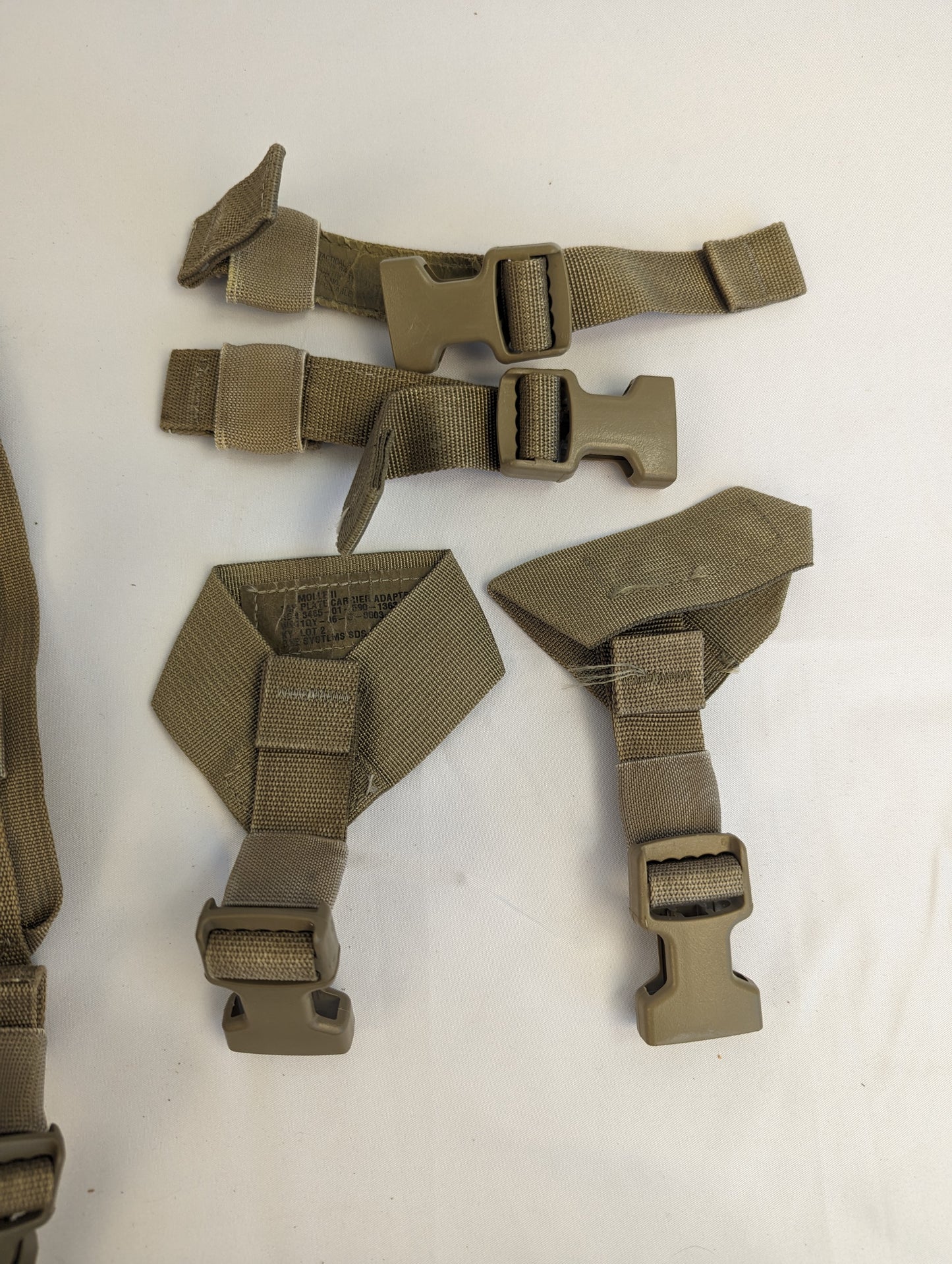 A set of detachable U.S. Military Surplus Coyote Brown webbing components, featuring quick-release plastic buckles and padded harness straps, laid flat on a white background.
