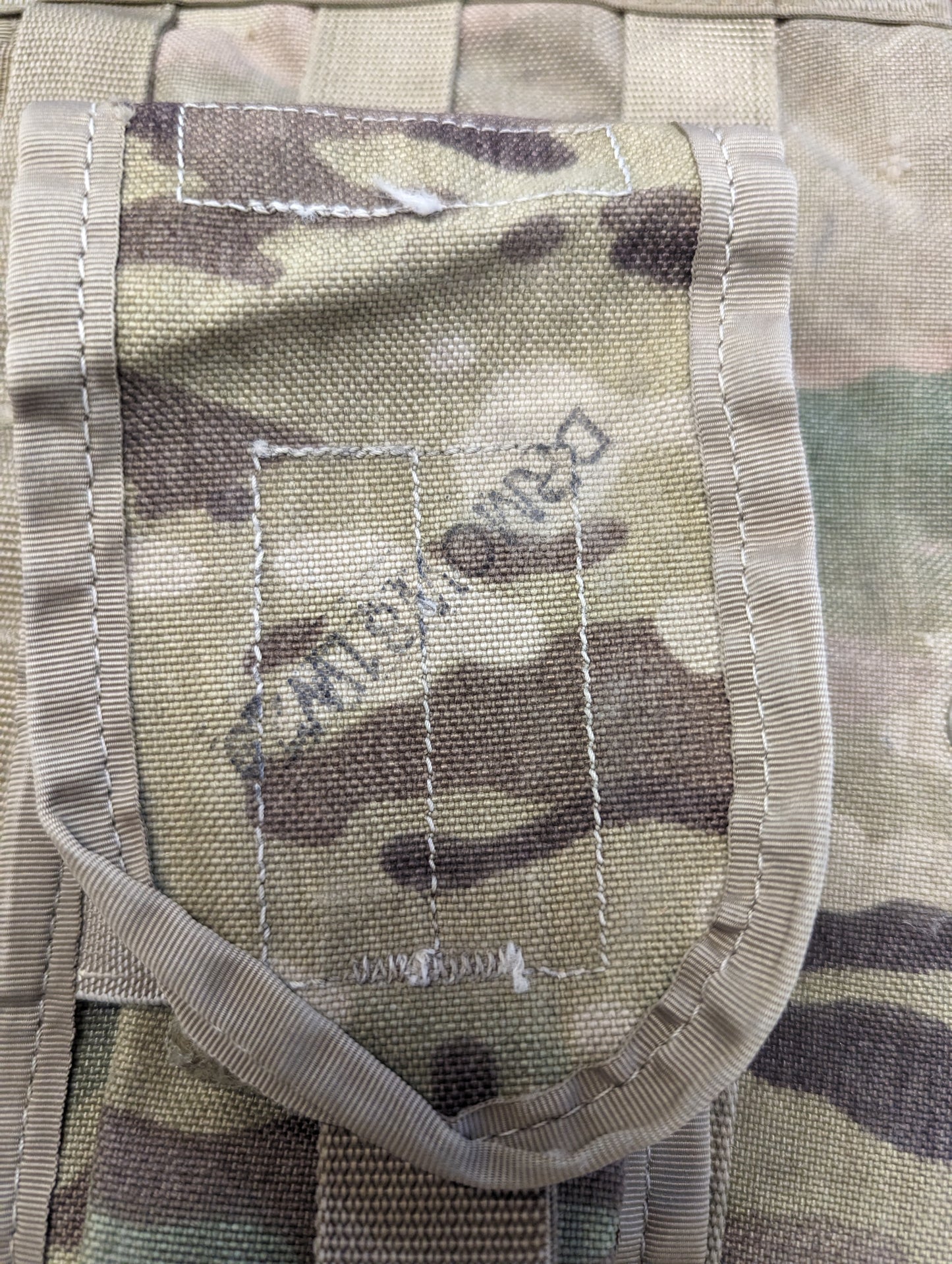 A close-up detail shot of the flap on an OCP/Multicam magazine pouch, prominently featuring the dark stenciled 'DRMO' marking, which indicates U.S. Military surplus.