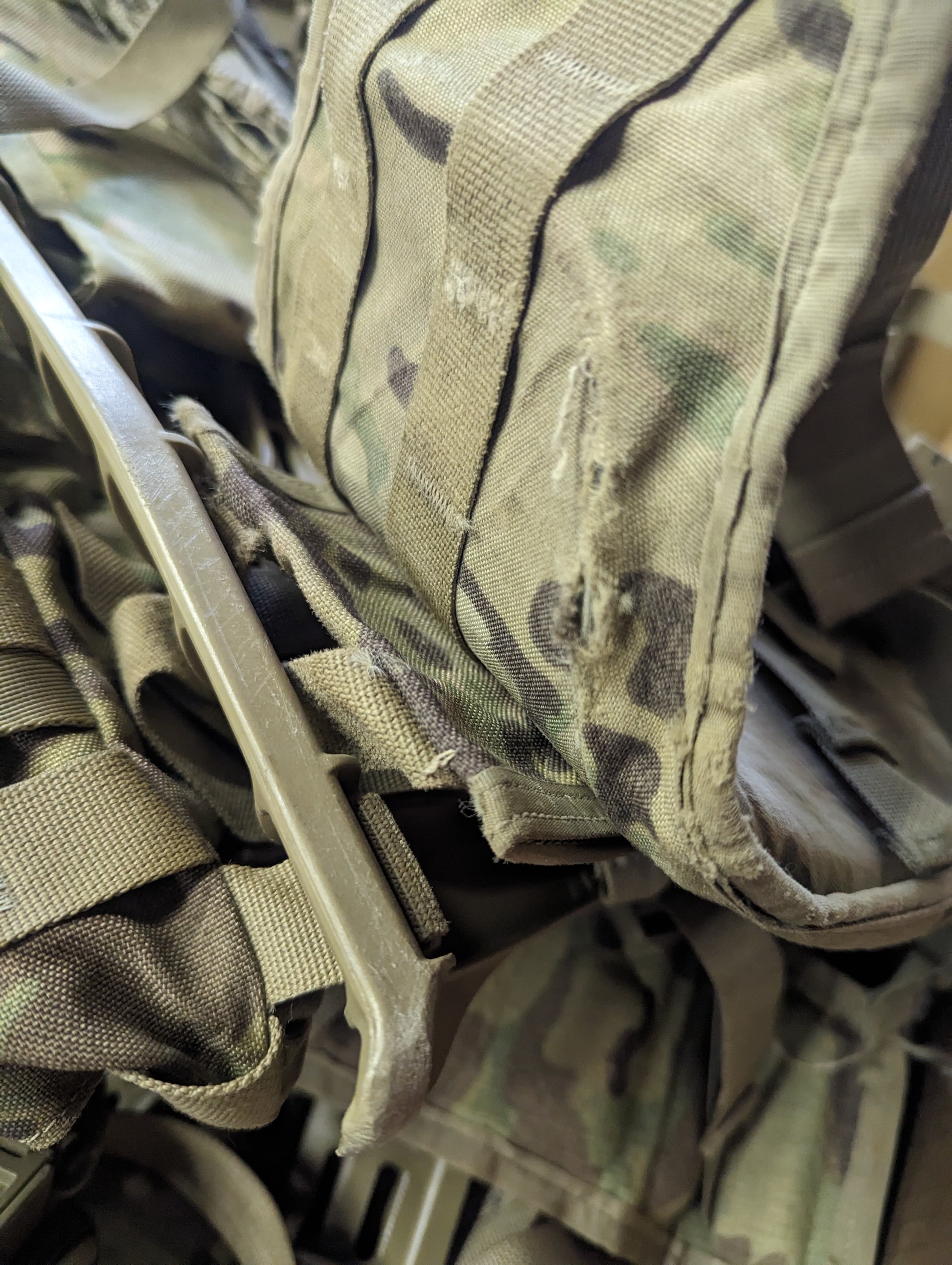 An extreme close-up of OCP/Multicam camouflage tactical gear, highlighting the fabric texture, MOLLE webbing, and a tan quick-release plastic buckle in the foreground.