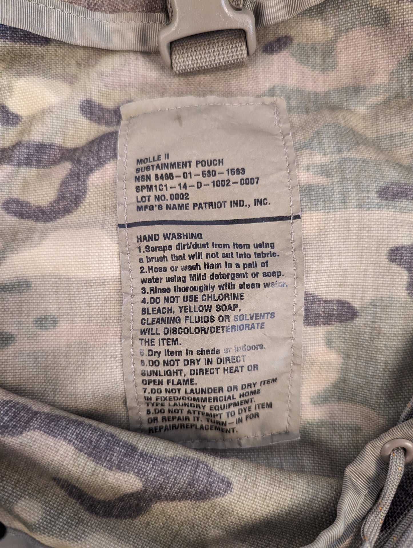 A close-up photograph of the official U.S. Military issue and care tag sewn into the OCP/Multicam Sustainment Pouch, displaying the product name, MOLLE II designation, and detailed laundering instructions.