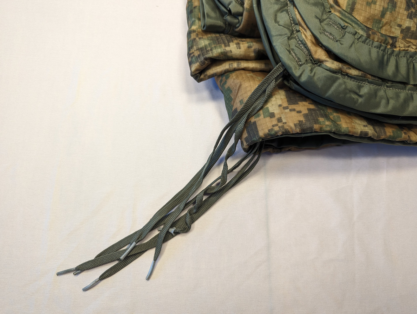 A close-up view of a U.S. Military Surplus Poncho Liner (Woobie) in MARPAT digital camouflage, folded over to display the solid golden-tan quilted interior lining and the olive drab edge binding.