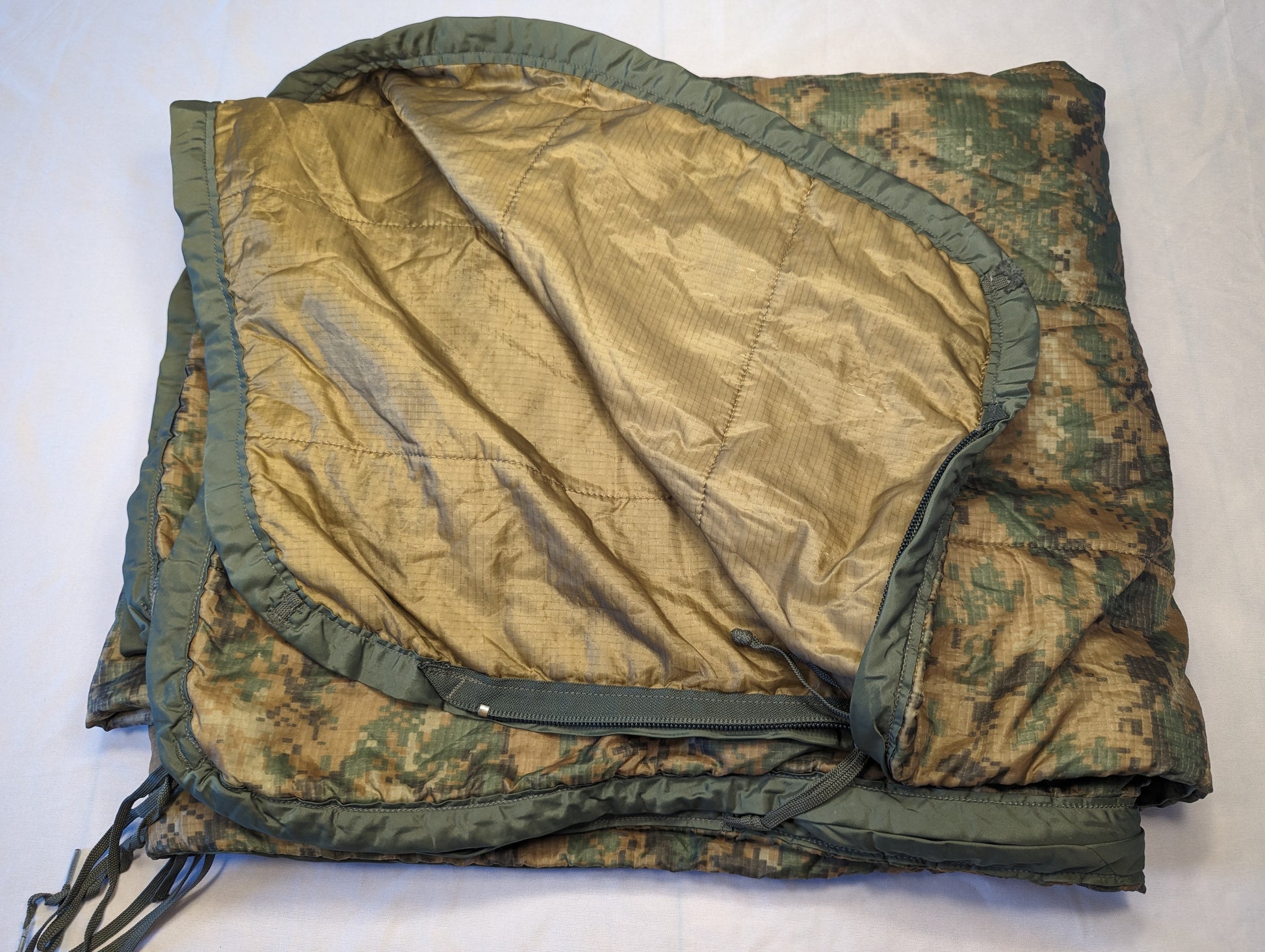 A close-up view of a U.S. Military Surplus Poncho Liner (Woobie) in MARPAT digital camouflage, folded over to display the solid golden-tan quilted interior lining and the olive drab edge binding.