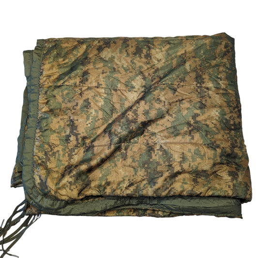 A U.S. Military Surplus Poncho Liner (Woobie) in MARPAT digital camouflage, laid flat and folded, displaying the quilted texture, edge binding, and attachment tie cords.