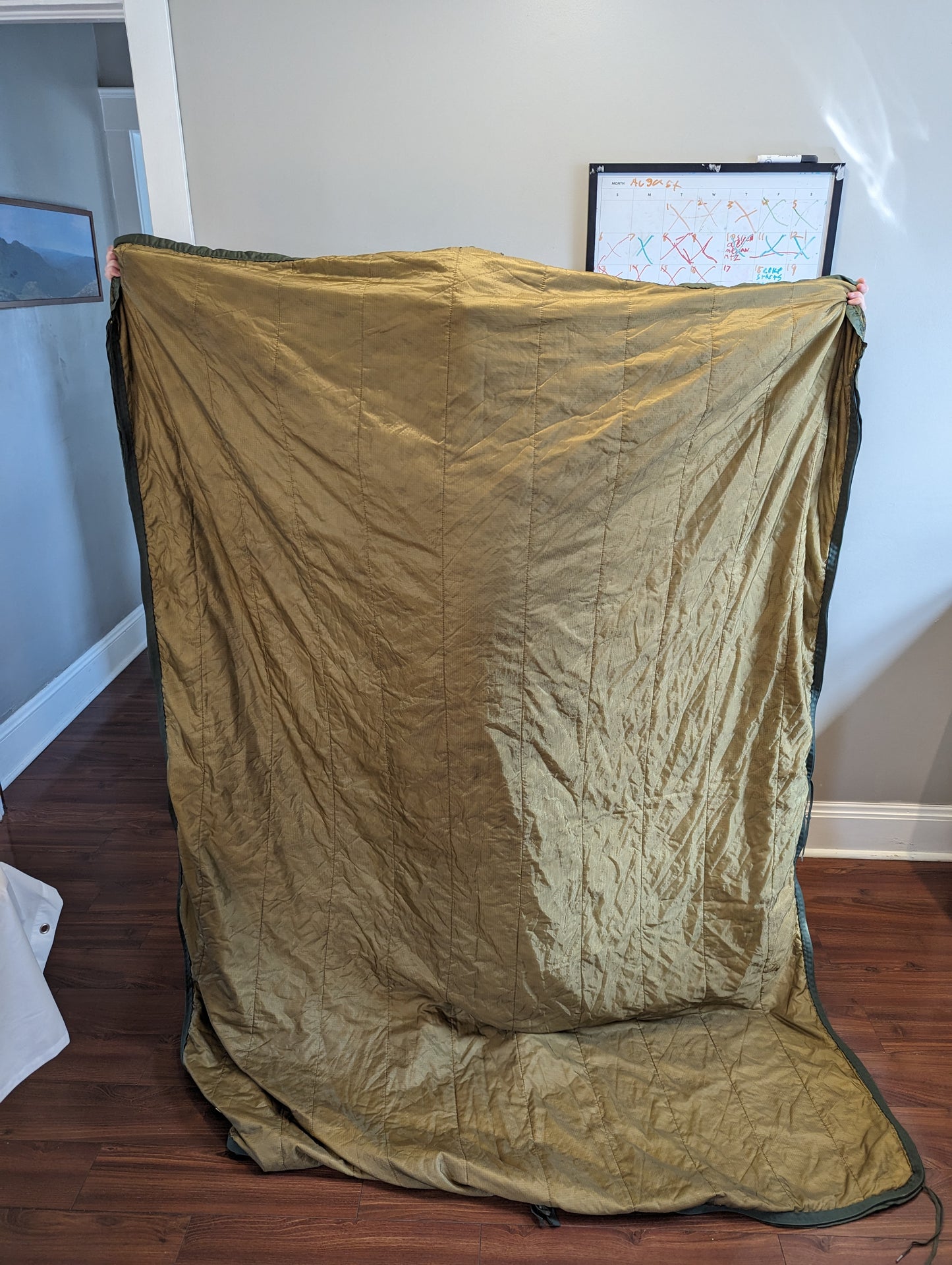 A full-size U.S. Military Surplus Poncho Liner (Woobie) in MARPAT digital camouflage, held up vertically by the edges to demonstrate its full dimensions and quilted pattern.