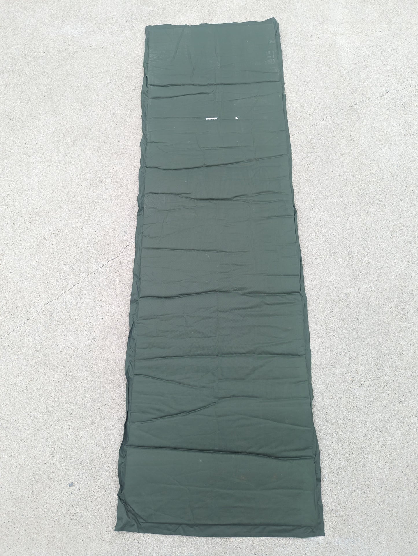 A full-length U.S. Military Surplus self-inflating sleeping mat in foliage green, laid flat vertically on a concrete surface, displaying the full size and ribbed texture.