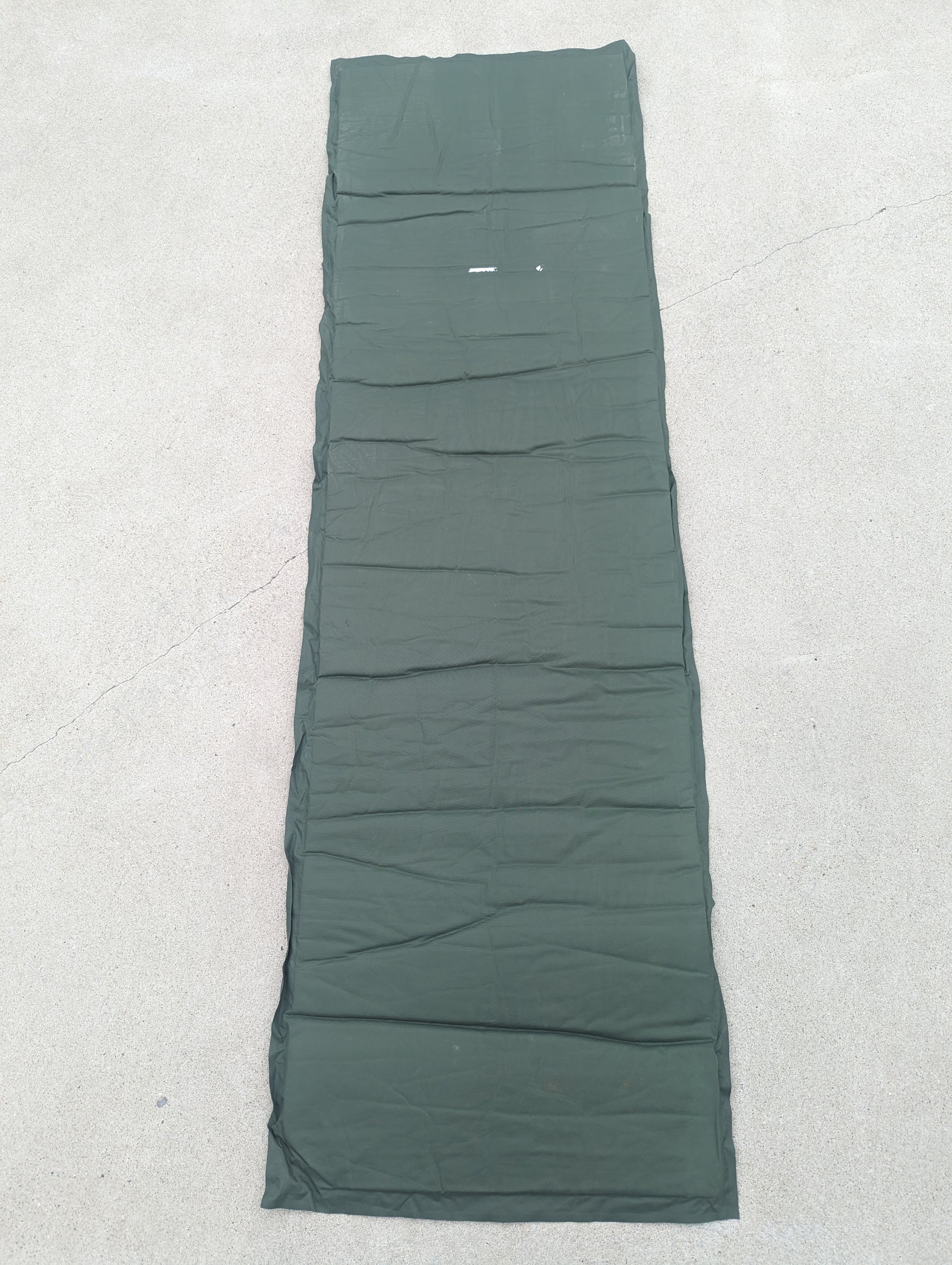 A full-length U.S. Military Surplus self-inflating sleeping mat in foliage green, laid flat vertically on a concrete surface, displaying the full size and ribbed texture.