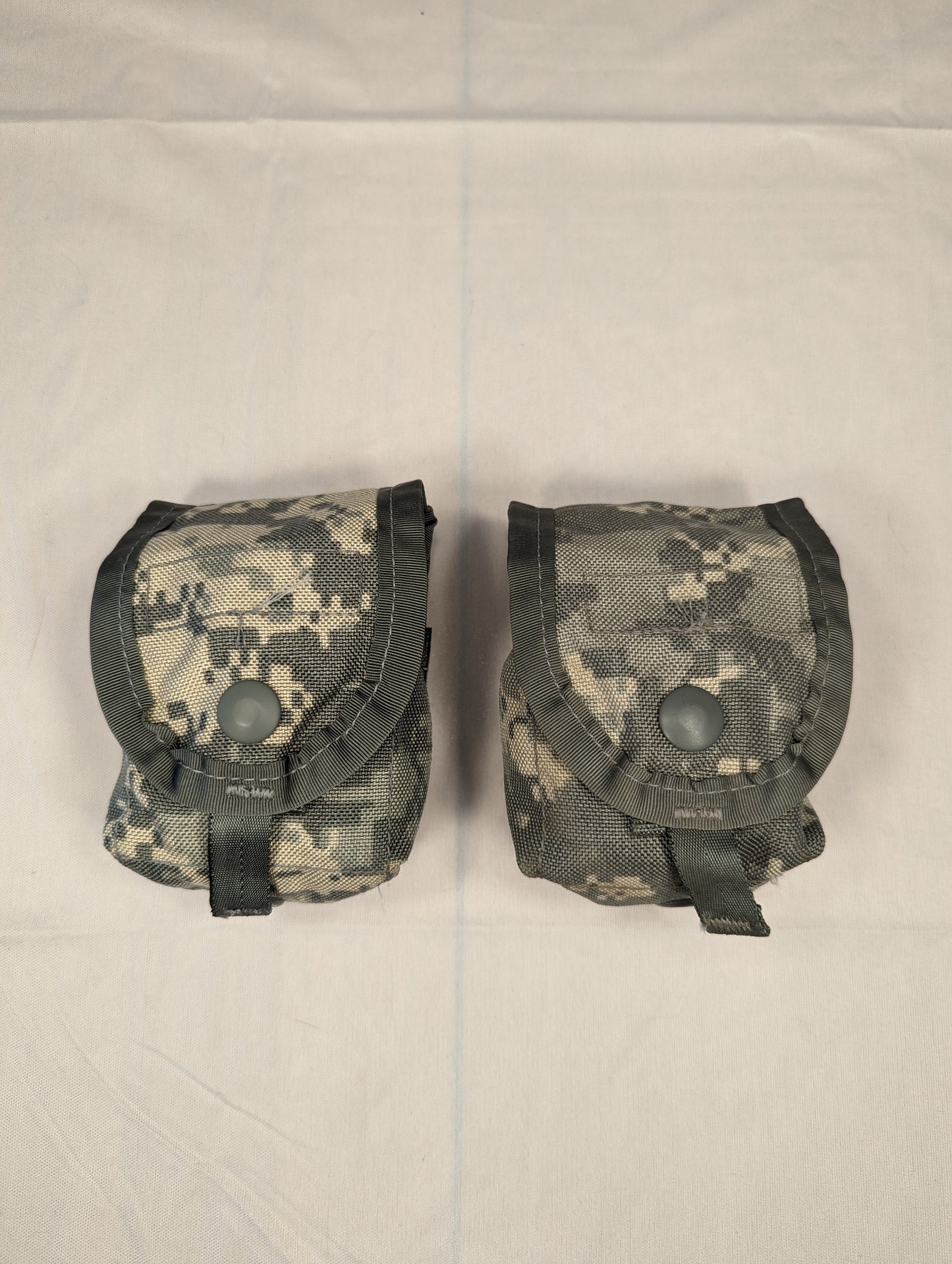 A pair of U.S. Military Surplus small tactical pouches in ACU digital camouflage, laid side-by-side, featuring snap-secured flap closures and horizontal webbing straps across the front.