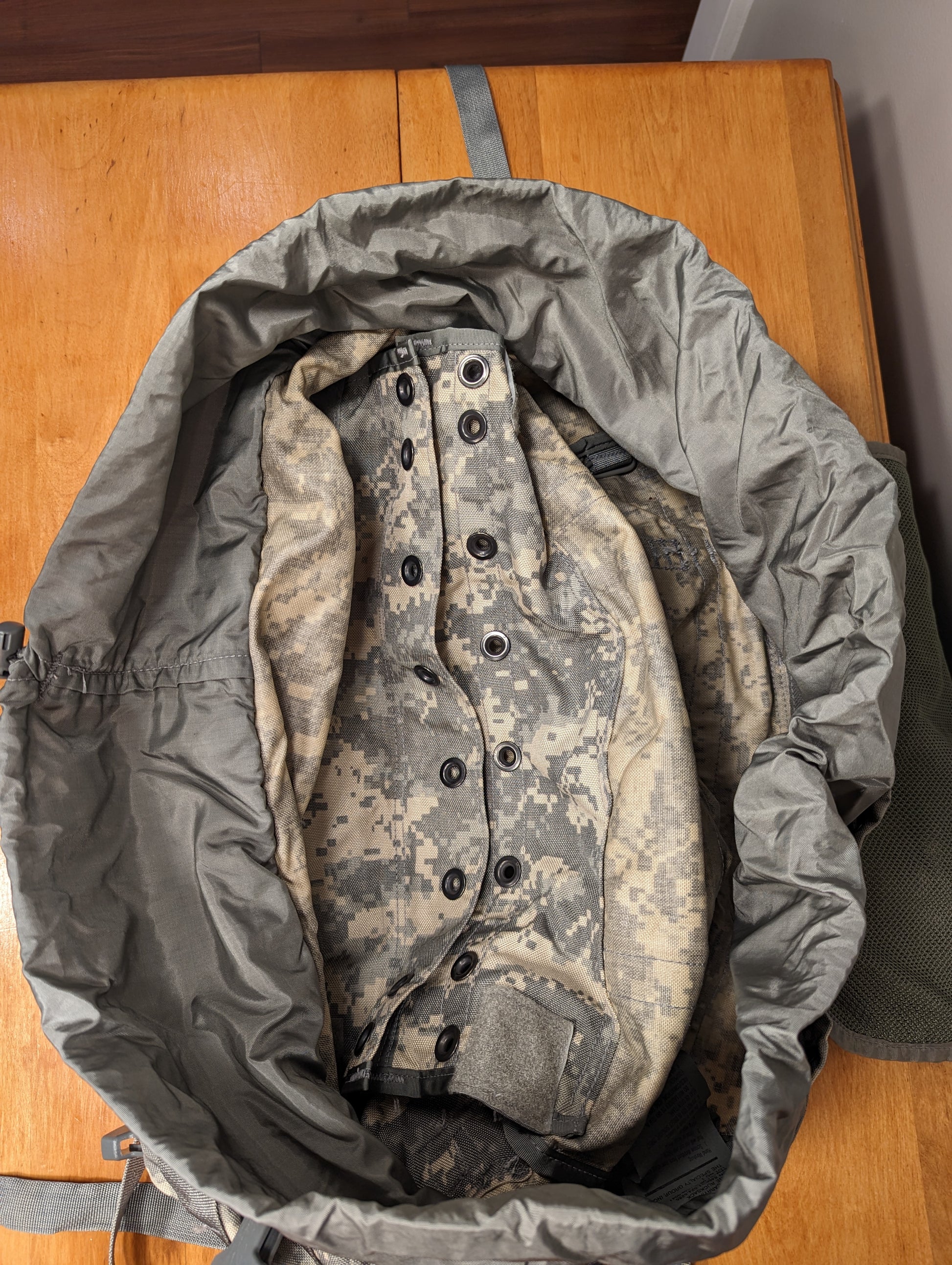 A close-up view of a U.S. Military surplus stuff sack containing a tightly rolled garment in desert digital camouflage, highlighting the packed texture and the drawstring opening.