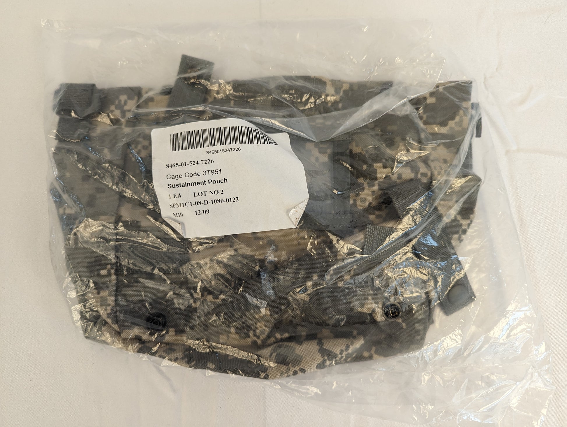 A new U.S. Military Surplus Sustainment Pouch in ACU digital camouflage, sealed inside clear plastic packaging, featuring the original issue label with product name, NSN, and contract details.