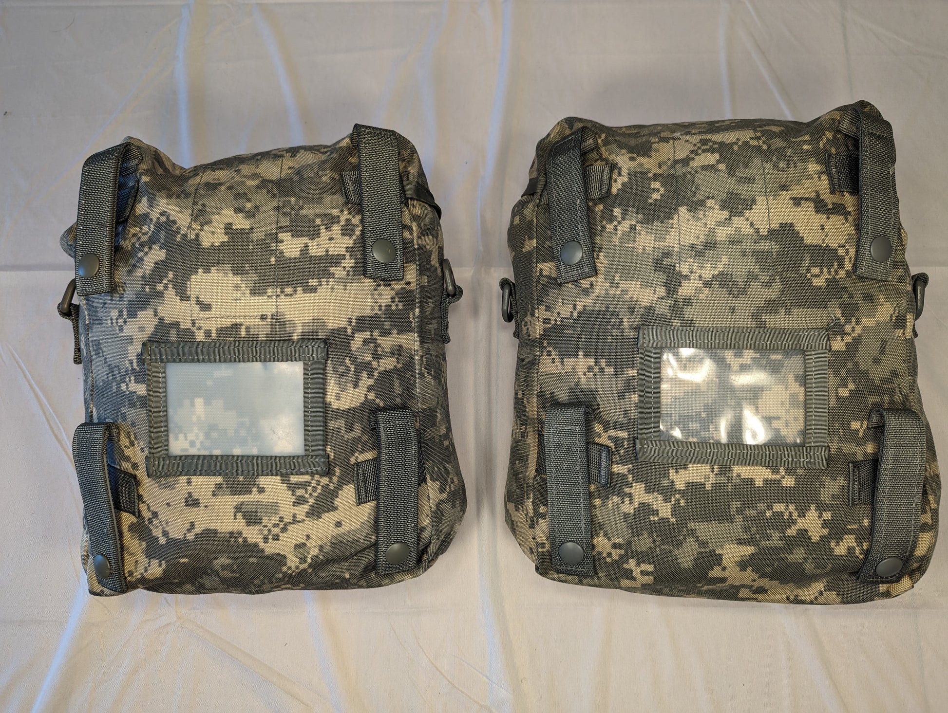 A back view of two U.S. Military Surplus Sustainment Pouches in ACU digital camouflage, laid side-by-side, displaying the vertical MOLLE attachment straps with snap closures and clear vinyl identification windows.