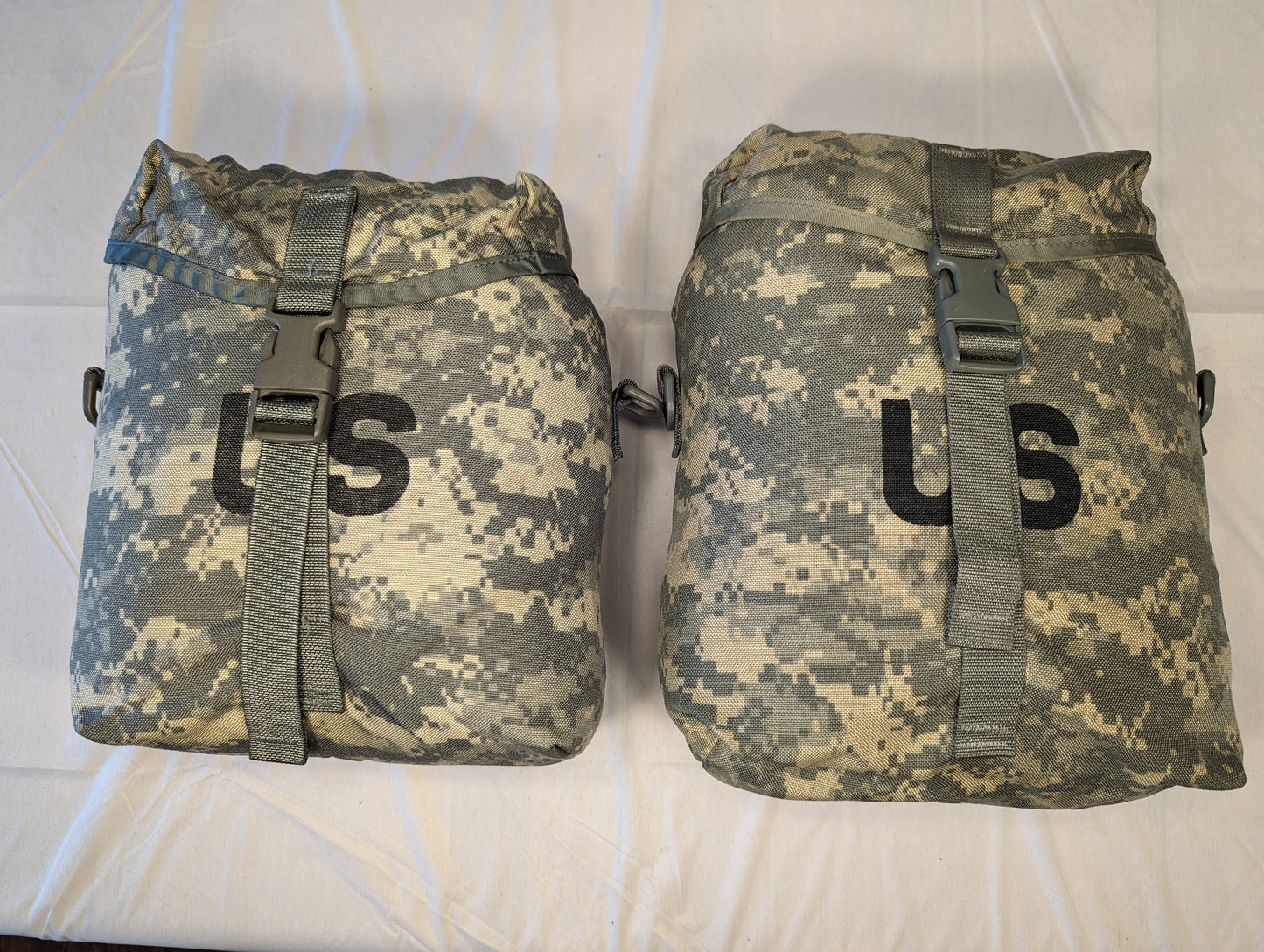 A studio shot of two U.S. Military Surplus Sustainment Pouches in ACU digital camouflage, standing upright side-by-side, featuring large stenciled 'US' markings and buckle-secured top flaps.