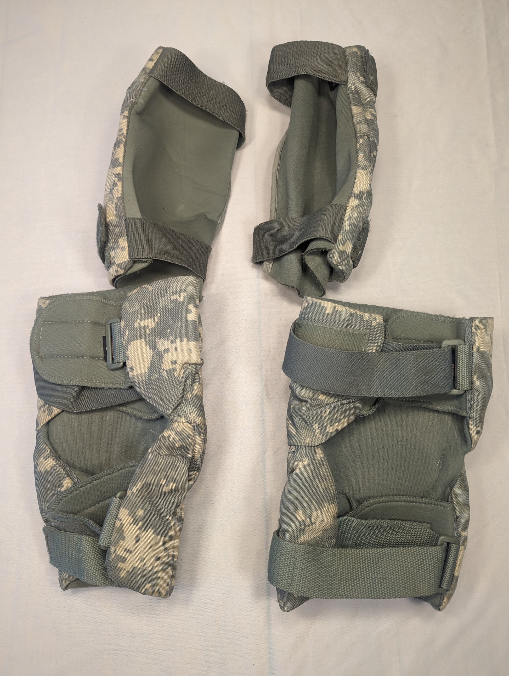 A set of four used U.S. Military tactical knee and elbow pads in ACU digital camouflage, laid out in a 2x2 grid on a white background, featuring dark gray hard plastic shells.