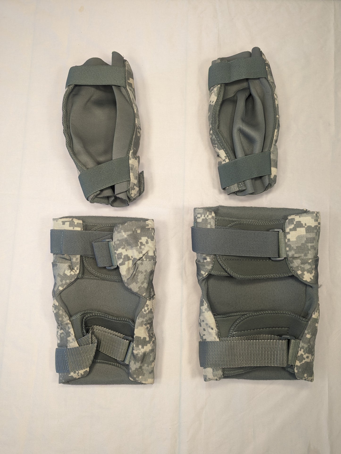 A set of four used U.S. Military tactical knee and elbow pads in ACU digital camouflage, laid out on a white background, featuring dark olive green hard plastic shells.