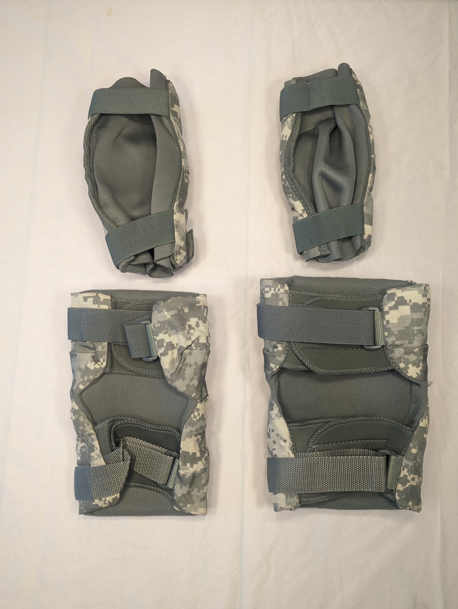 A set of four used U.S. Military tactical knee and elbow pads in ACU digital camouflage, laid out on a white background, featuring dark olive green hard plastic shells.