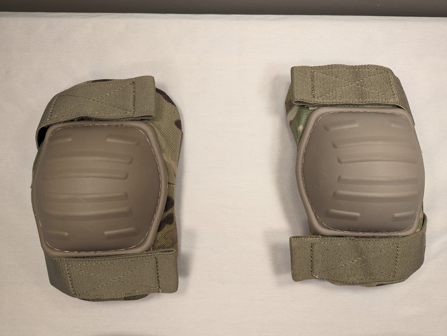 A pair of U.S. Military tactical elbow pads in OCP/Multicam camouflage, laid flat on a white background, featuring tan hard plastic protective shells and adjustable hook-and-loop straps.