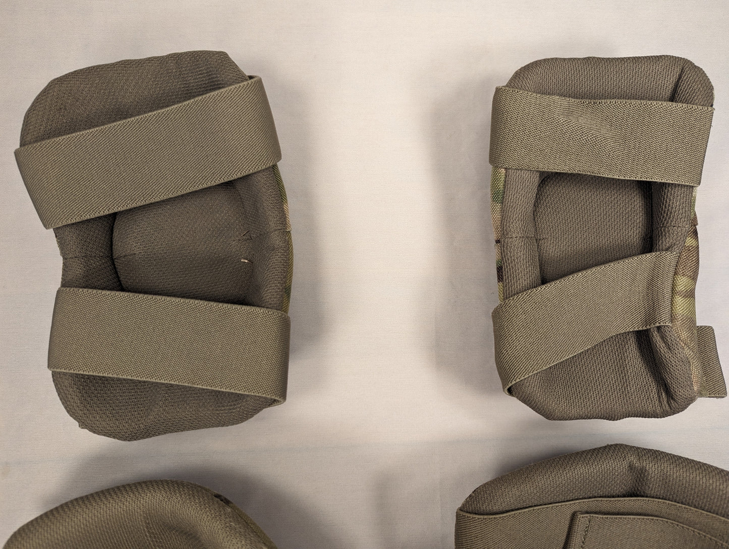 A close-up view of the interior of a complete set of U.S. Military tactical knee and elbow pads, displaying the olive drab padded lining and OCP/Multicam camouflage straps.