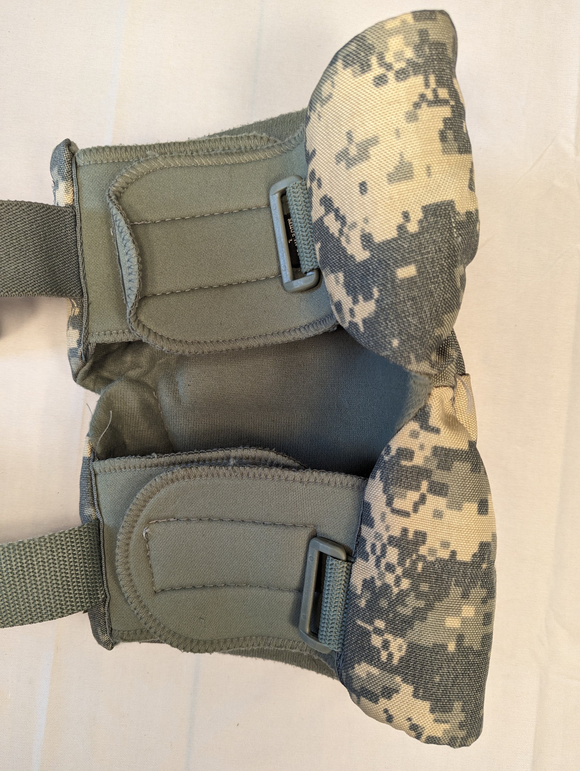 A pair of U.S. Military tactical knee pads in ACU digital camouflage, laid flat side-by-side on a white background, featuring foliage green hard plastic protective shells secured with rivets.