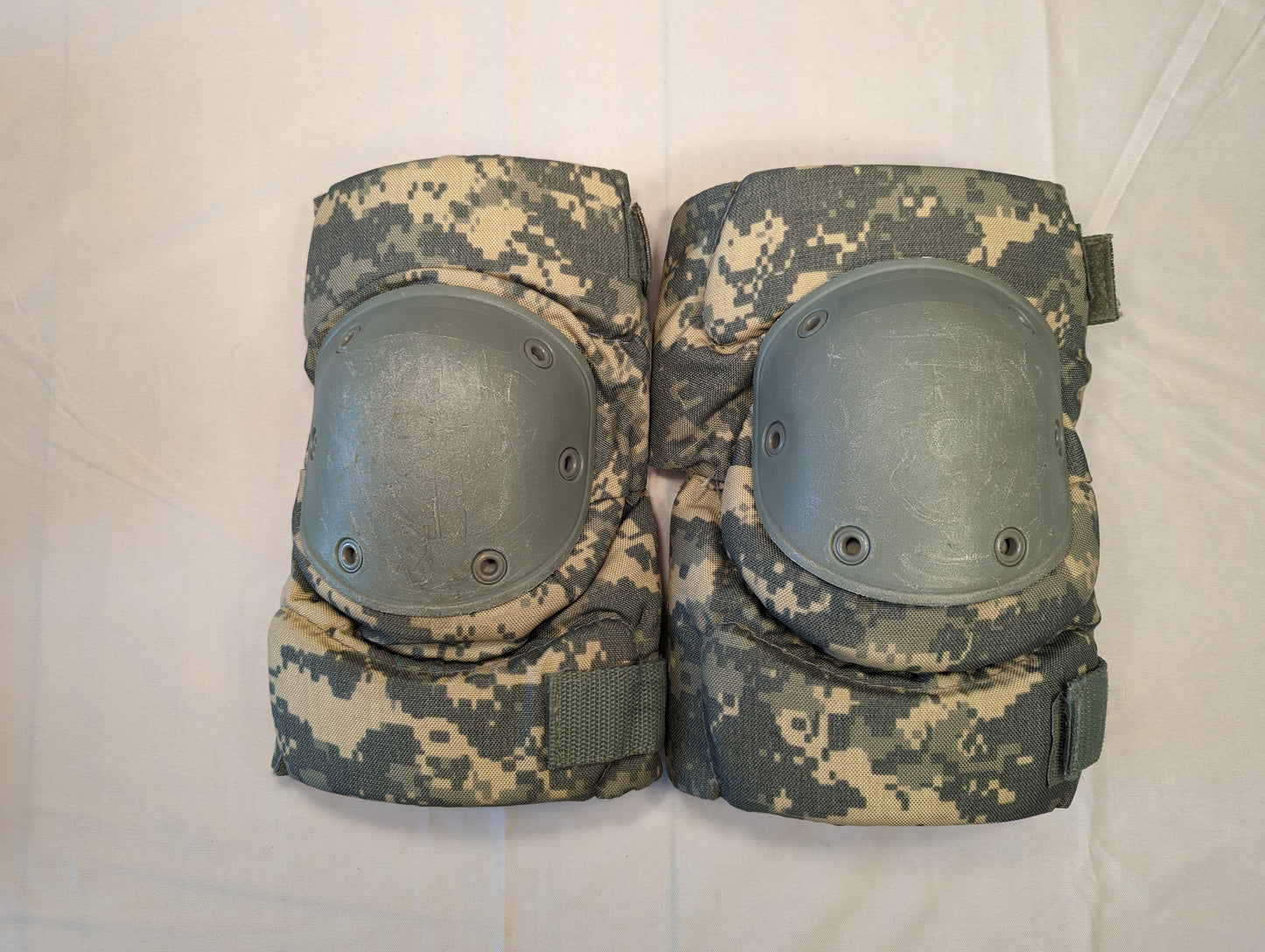 A pair of U.S. Military tactical knee pads in ACU digital camouflage, laid flat side-by-side on a white background, featuring foliage green hard plastic protective shells secured with rivets.