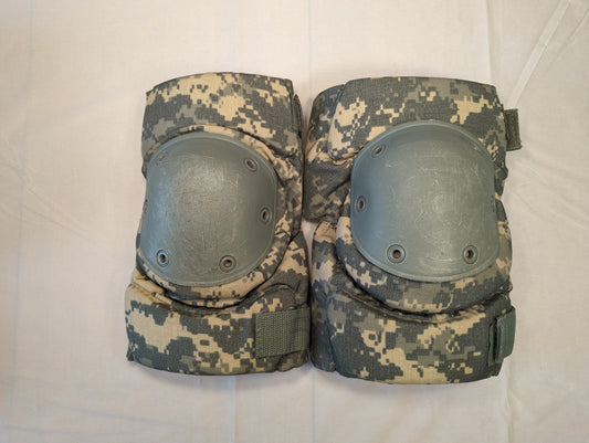 A pair of U.S. Military tactical knee pads in ACU digital camouflage, laid flat side-by-side on a white background, featuring foliage green hard plastic protective shells secured with rivets.