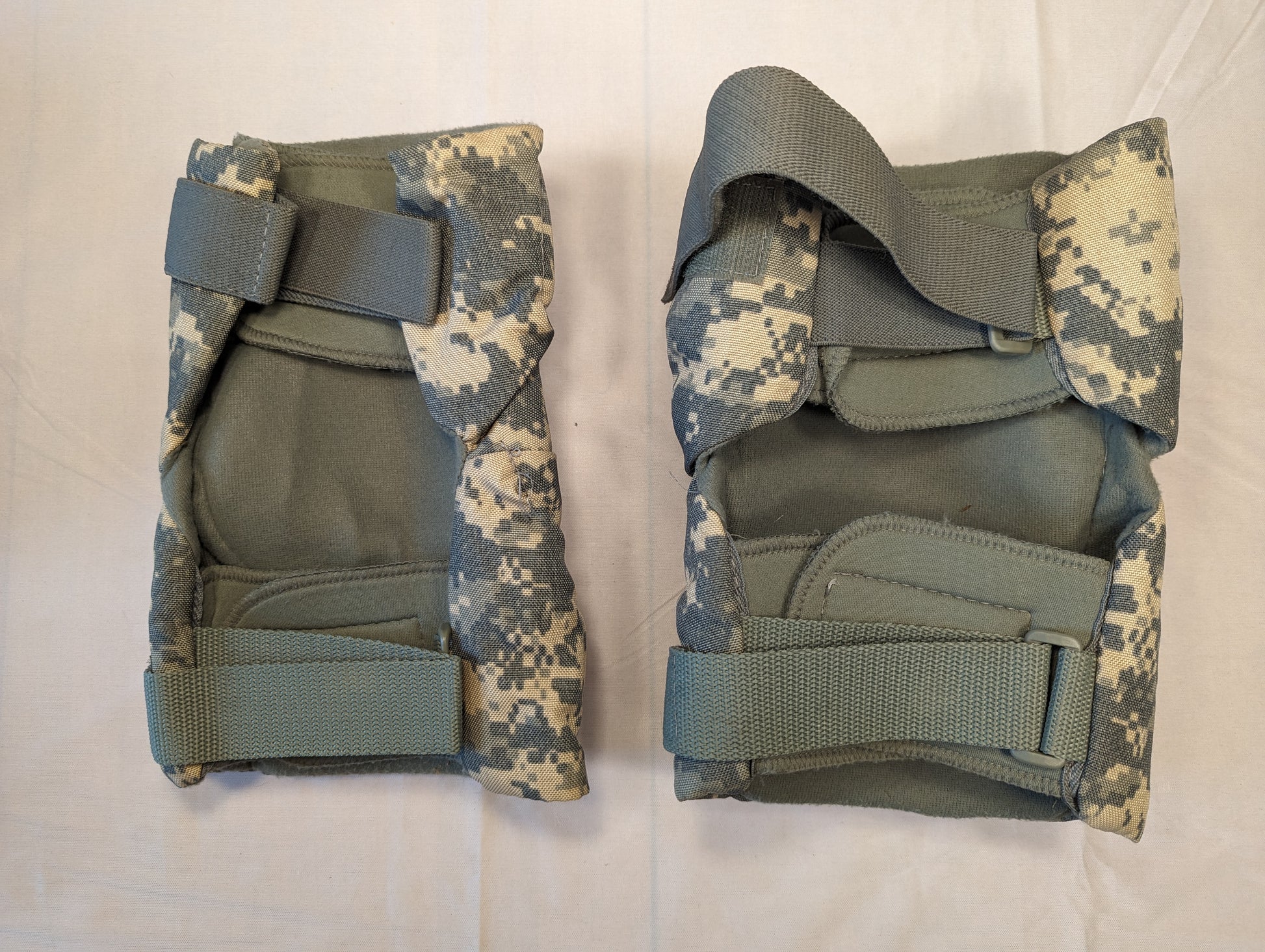 A pair of U.S. Military tactical knee pads in ACU digital camouflage, laid flat side-by-side on a white background, featuring foliage green hard plastic protective shells and adjustable straps.