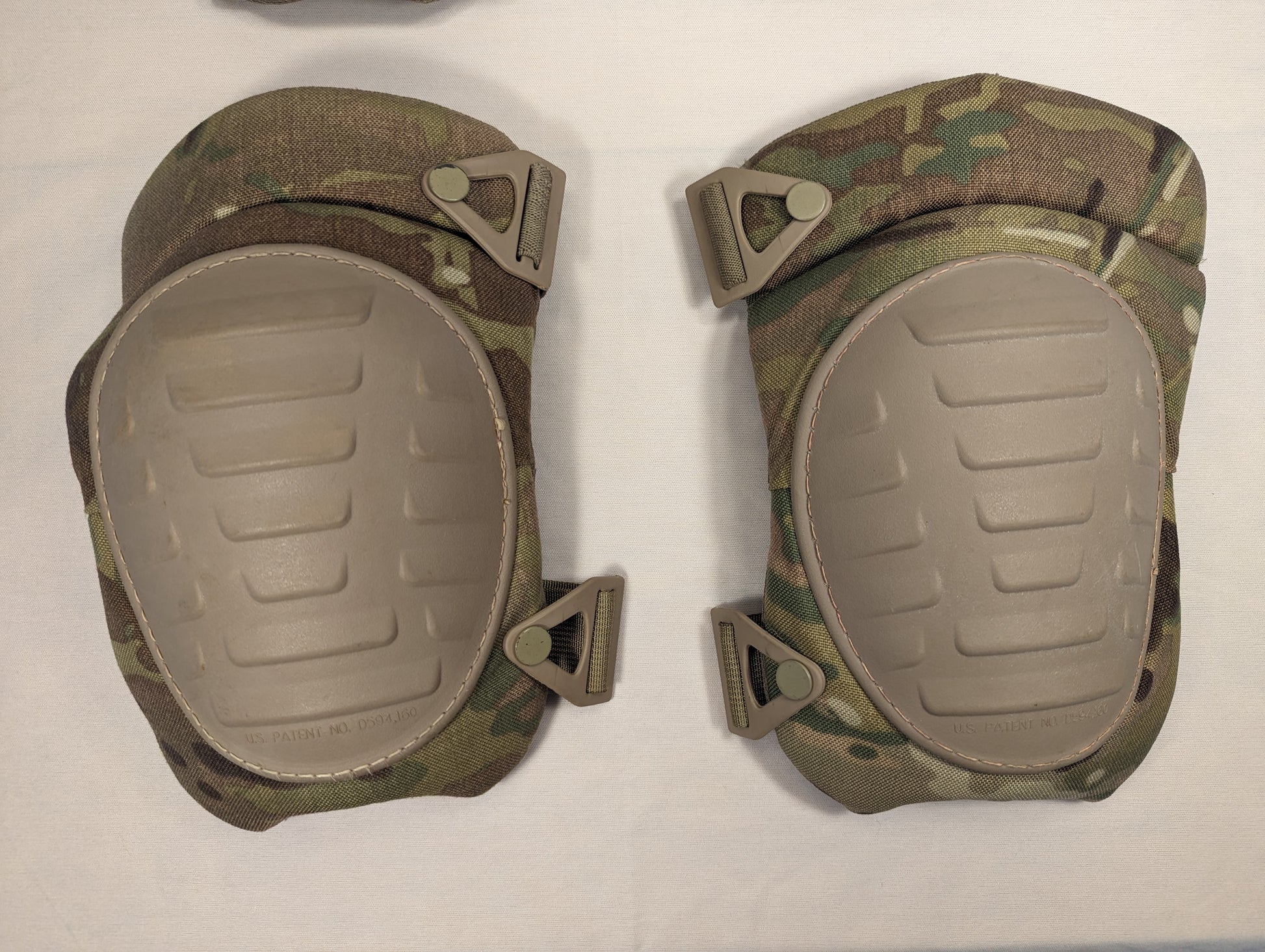 A pair of U.S. Military tactical knee pads in OCP/Multicam camouflage, featuring tan hard plastic shells and triangular strap attachments, laid flat on a white background.