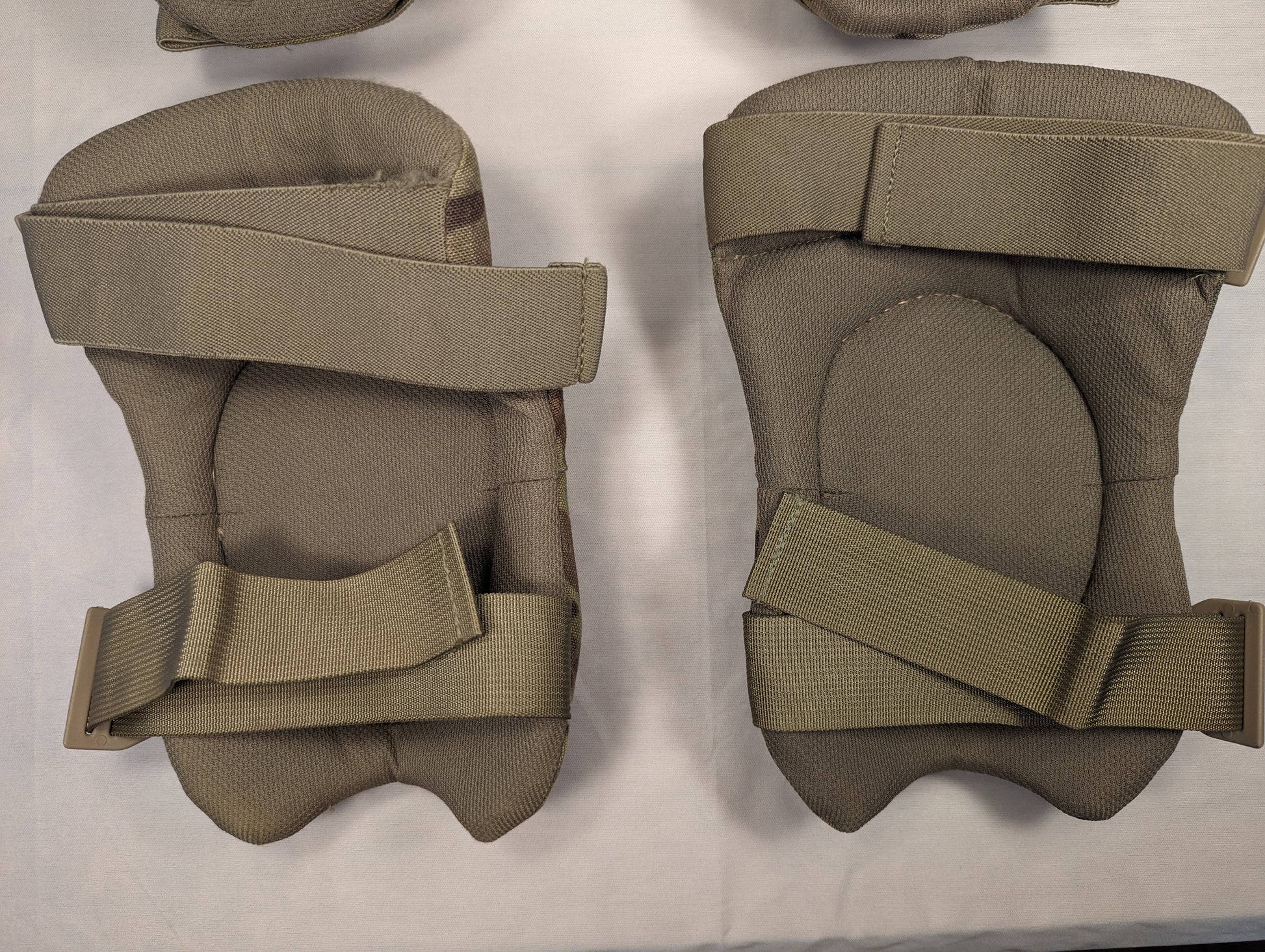 A pair of U.S. Military tactical knee pads in olive drab green, laid flat on a white background, featuring a fabric-covered hard protective shell and adjustable hook-and-loop straps.