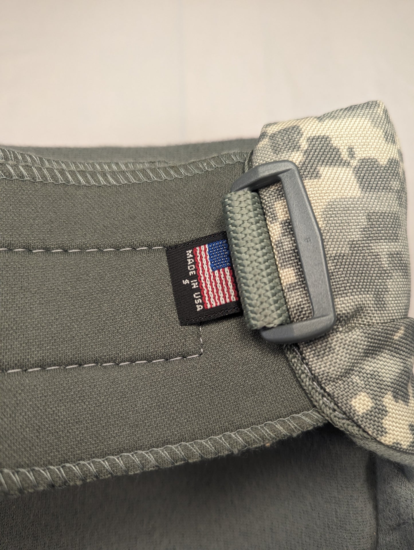 A close-up of the U.S. flag tag sewn into the foliage green strap of a tactical pad, prominently featuring the 'MADE IN U.S.A.' text next to a plastic adjustment buckle.