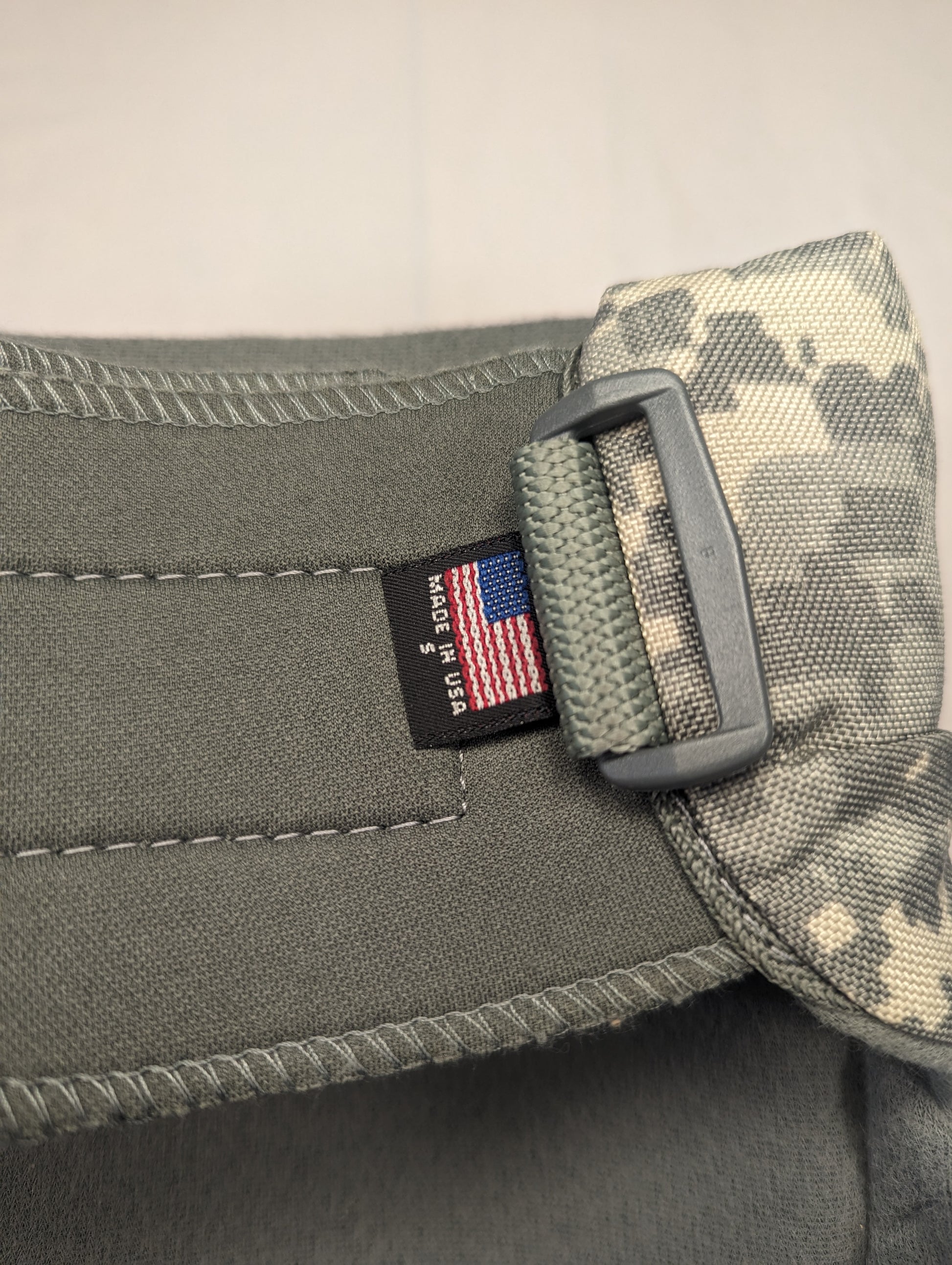 A close-up of the U.S. flag tag sewn into the foliage green strap of a tactical pad, prominently featuring the 'MADE IN U.S.A.' text next to a plastic adjustment buckle.