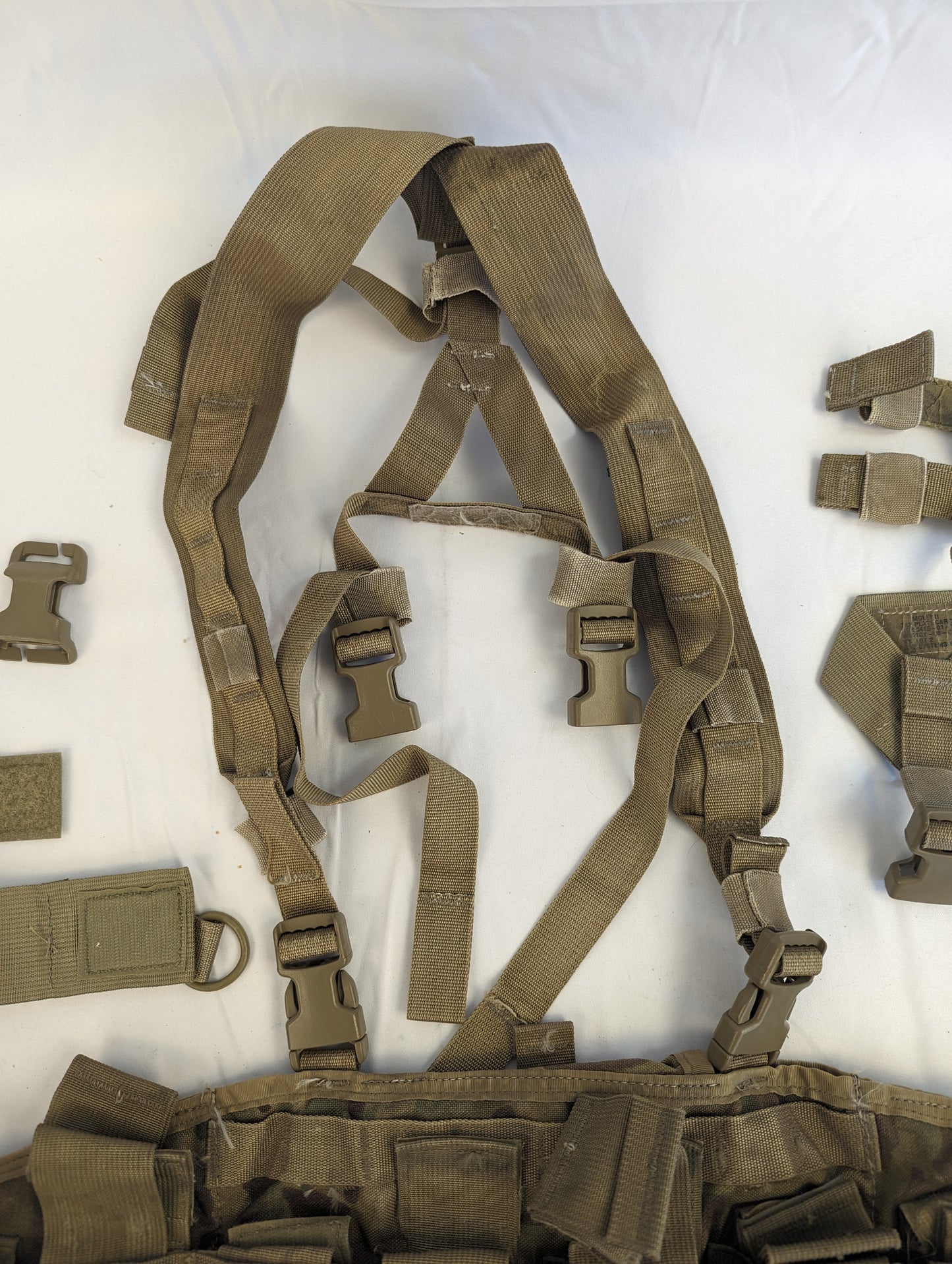 A set of Coyote Brown tactical webbing components laid flat, including a padded shoulder harness, adjustment straps, quick-release buckles, and accessory pouches for a MOLLE chest rig or vest.